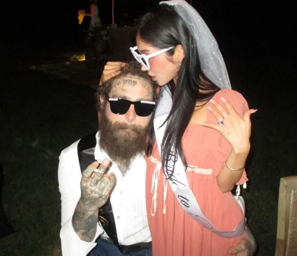 A heavily tattooed man in sunglasses with a beard and a woman in a wedding veil and 
