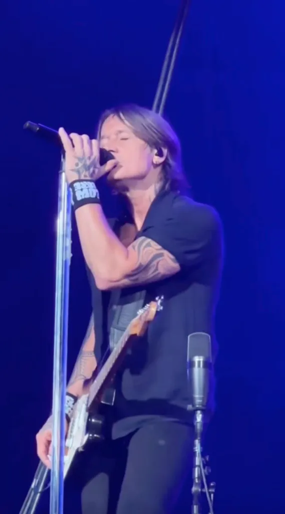 Keith Urban performing live with a microphone and guitar.