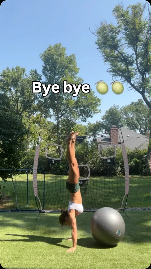 A woman doing a handstand in front of a baseball net.