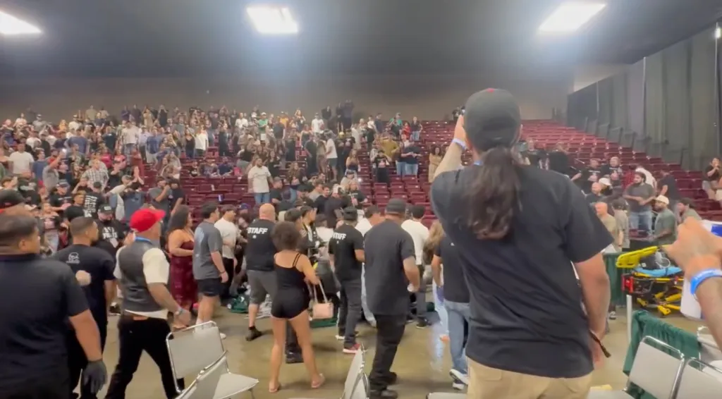 A large crowd of people standing and cheering in an auditorium, with some staff visible in the foreground.