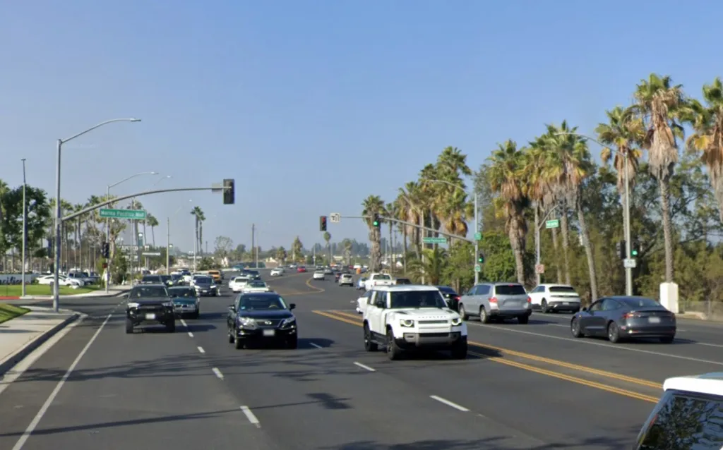 Traffic on a multi-lane street with palm trees lining the road and a green sign for 