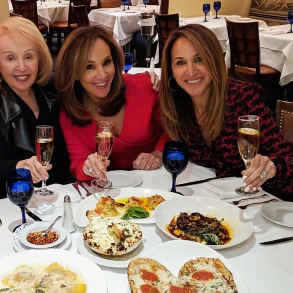 Rosanna Scotto, her sister Eliana, and mother Marion toast champagne at a dinner table filled with food.