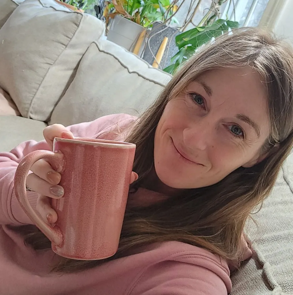 Ashley Taunton holding a pink mug while smiling at the camera.