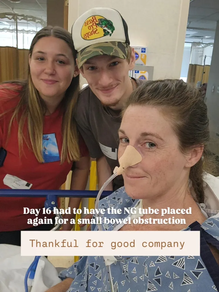 A woman with a nasal gastric tube in a hospital bed is visited by two younger people.