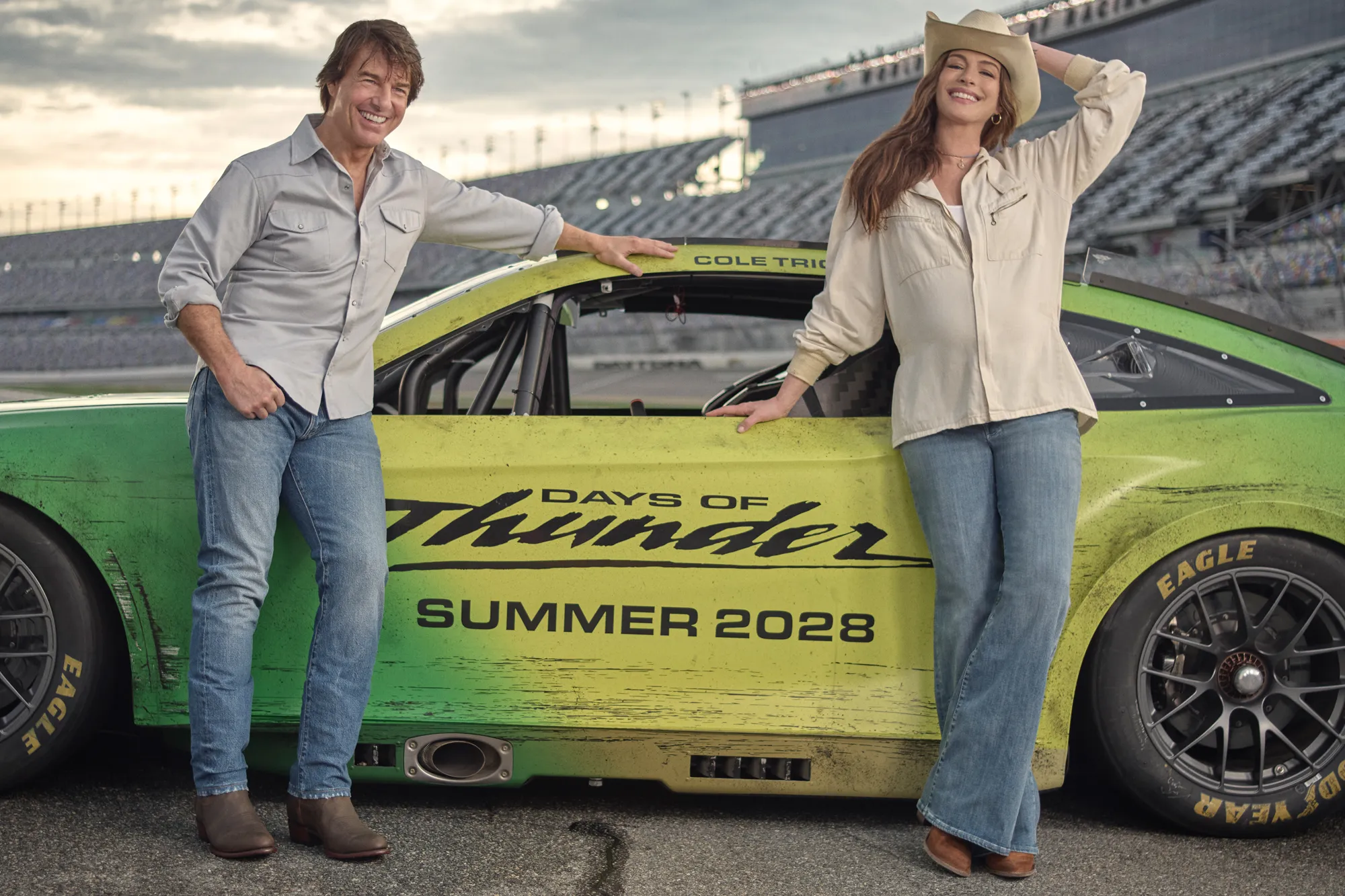 Tom Cruise and Anne Hathaway standing next to a green race car with 