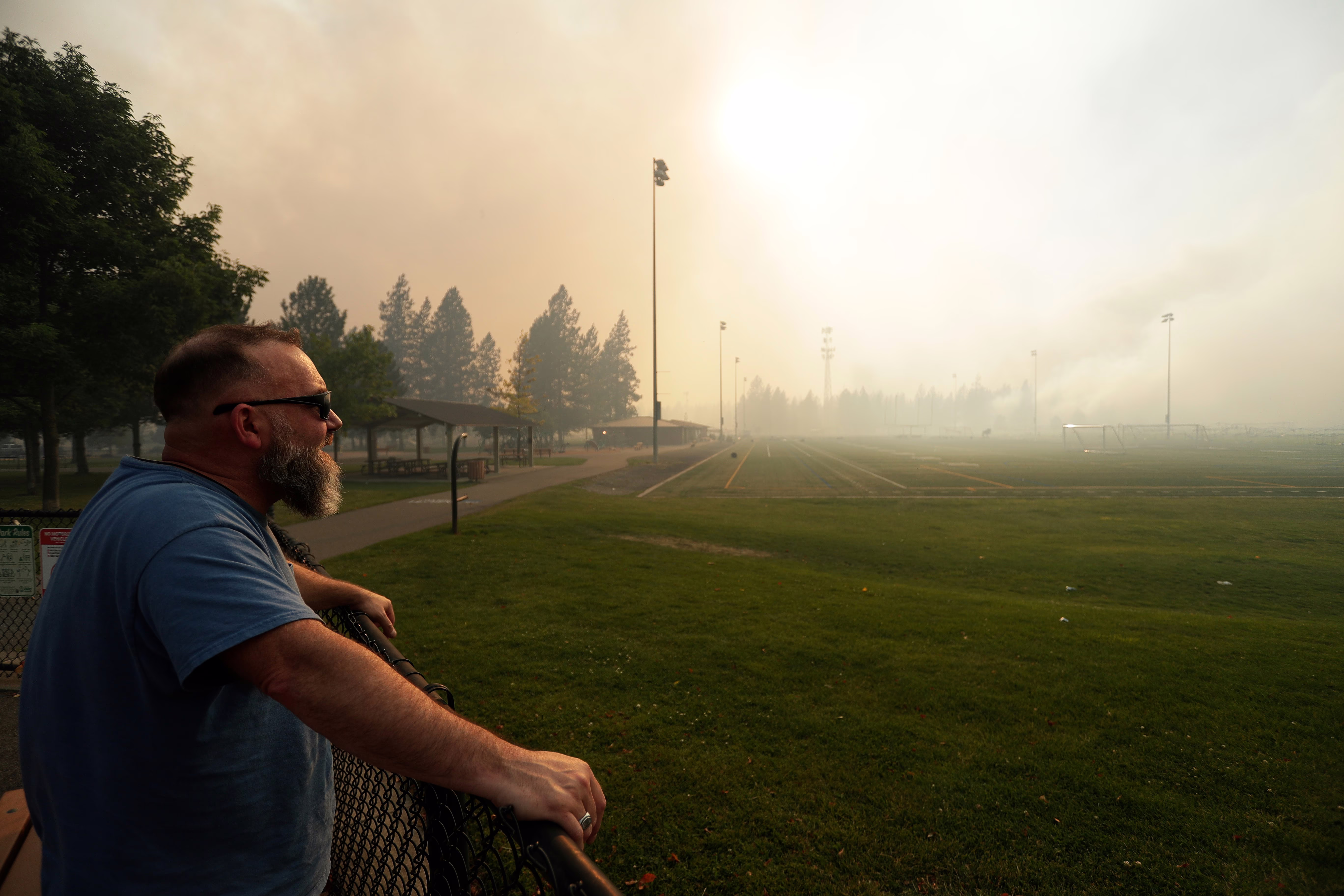 A person watches as a wildfire burns near a sports field.