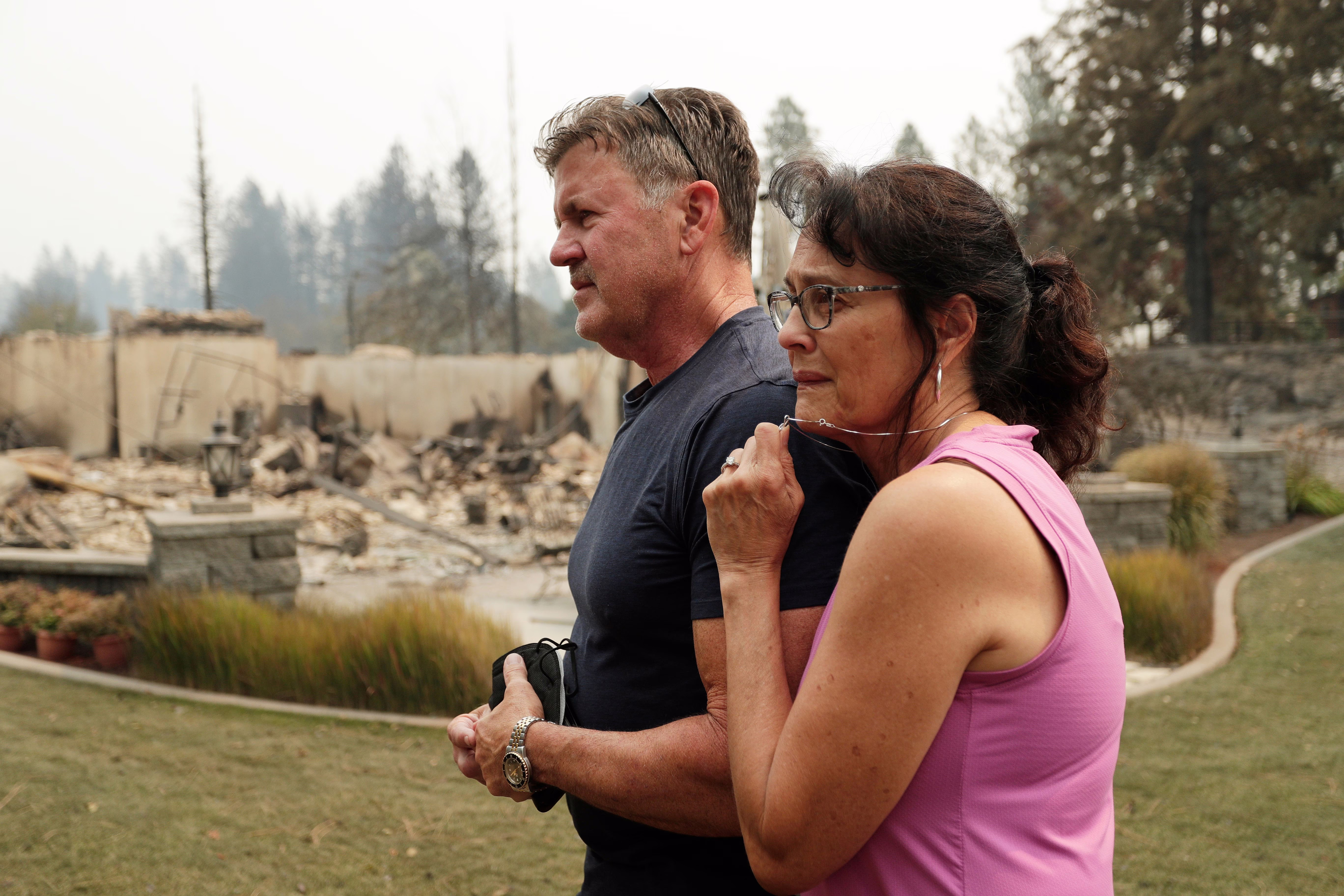 A husband and wife stand together outside a burned house.