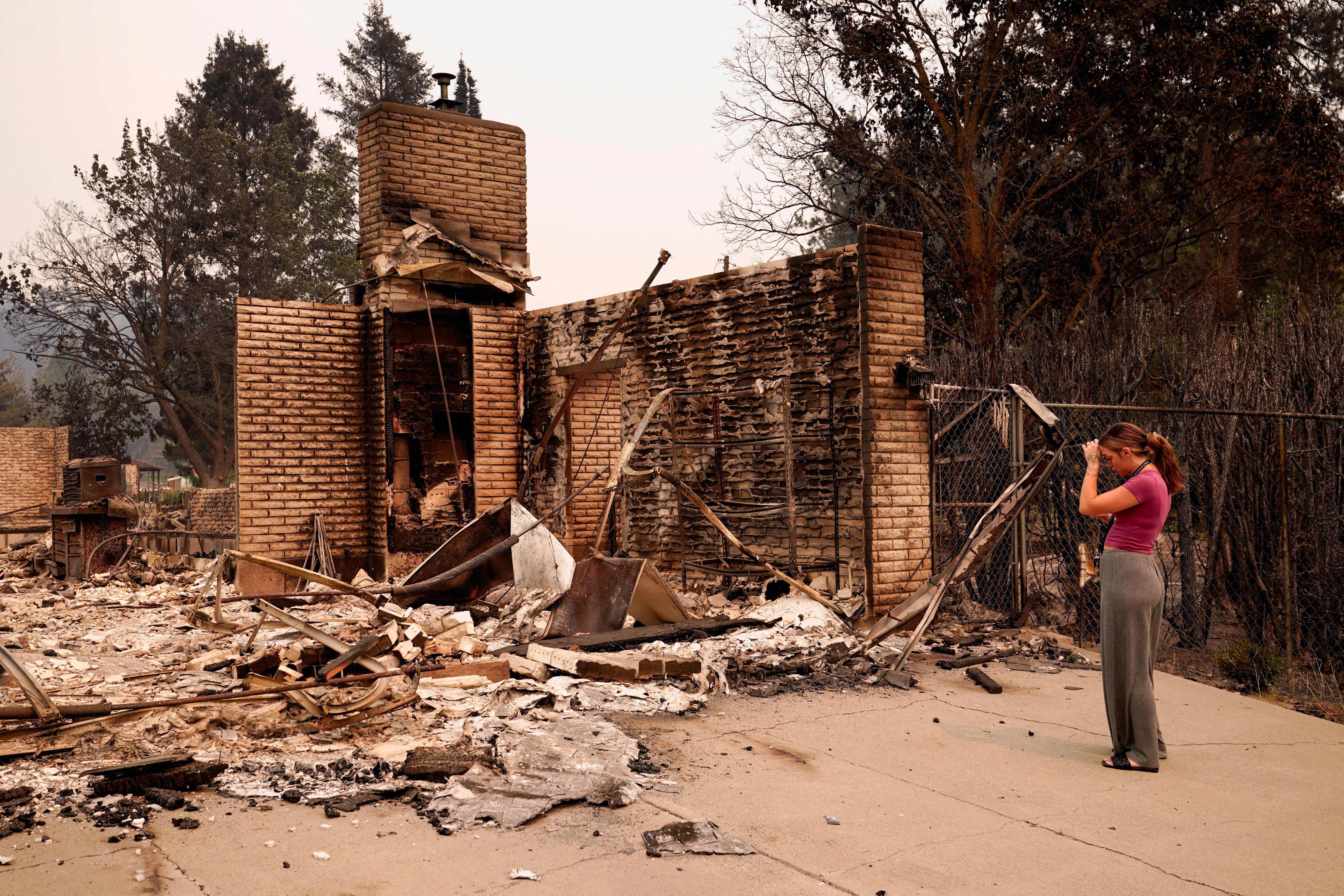 A woman stands in front of the rubble of a burned house.