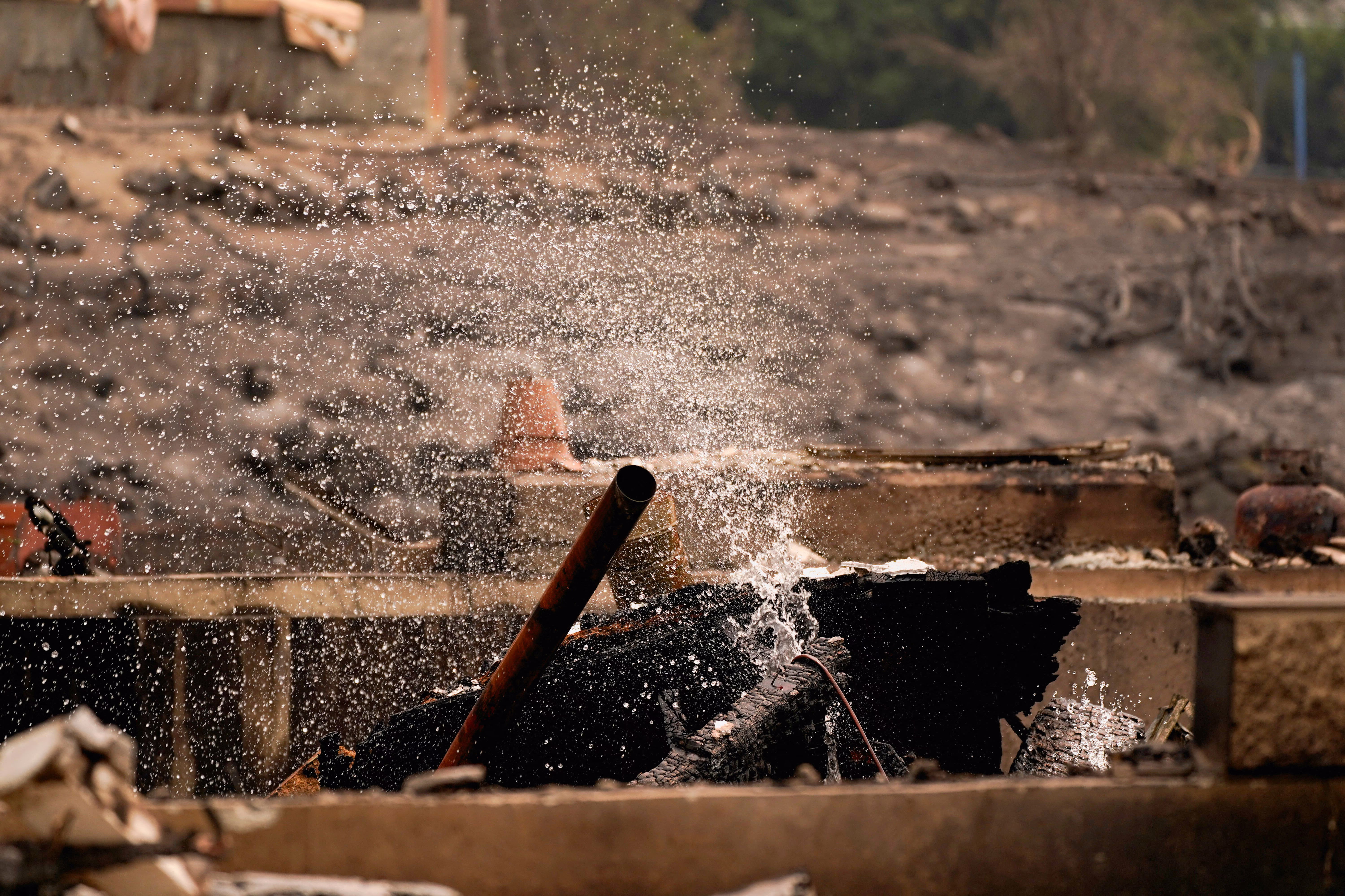 Water sprays over the charred remains of a burned property.
