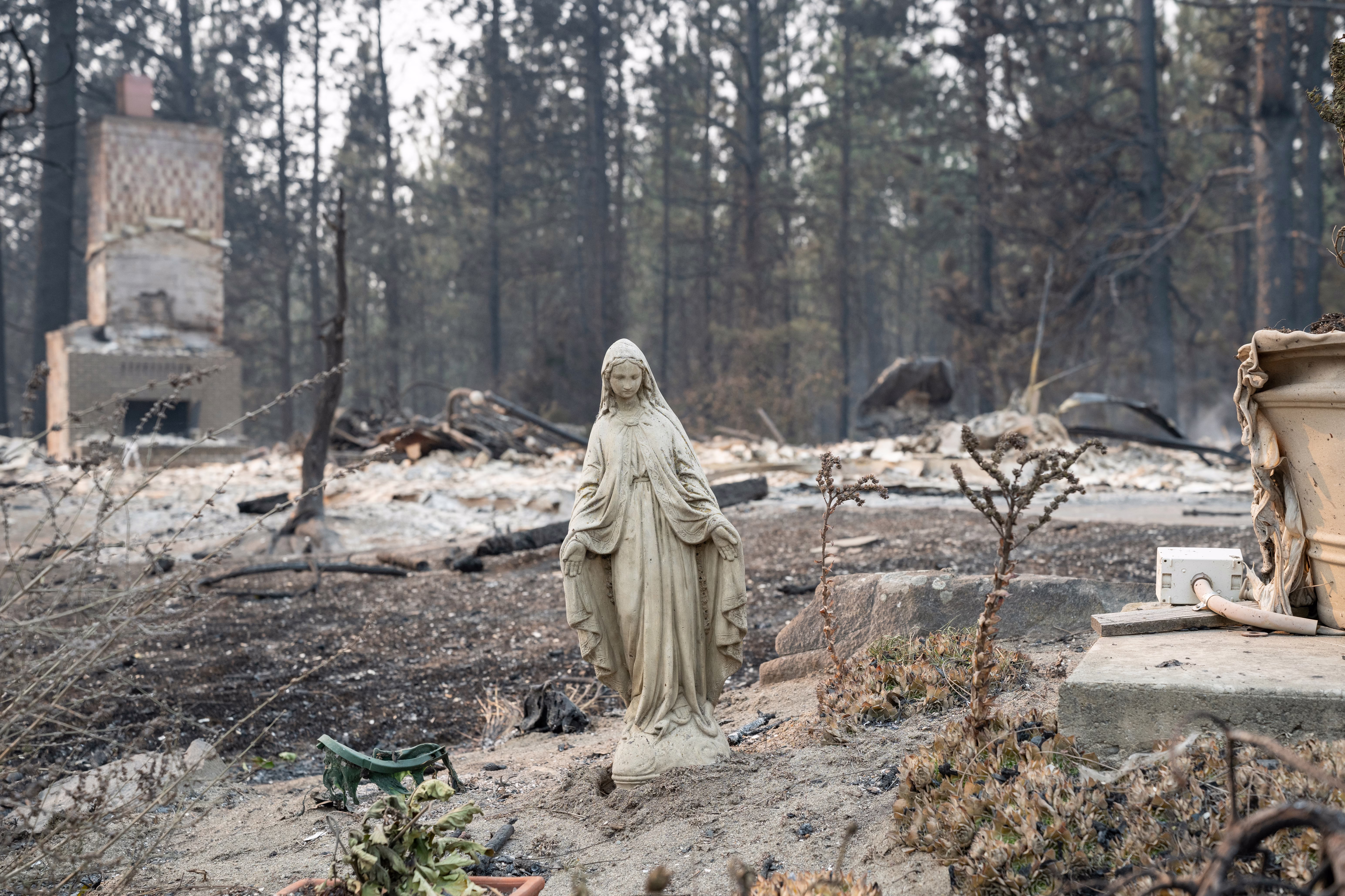 A relatively unscathed Virgin Mary statue stands in a burned-out neighborhood.