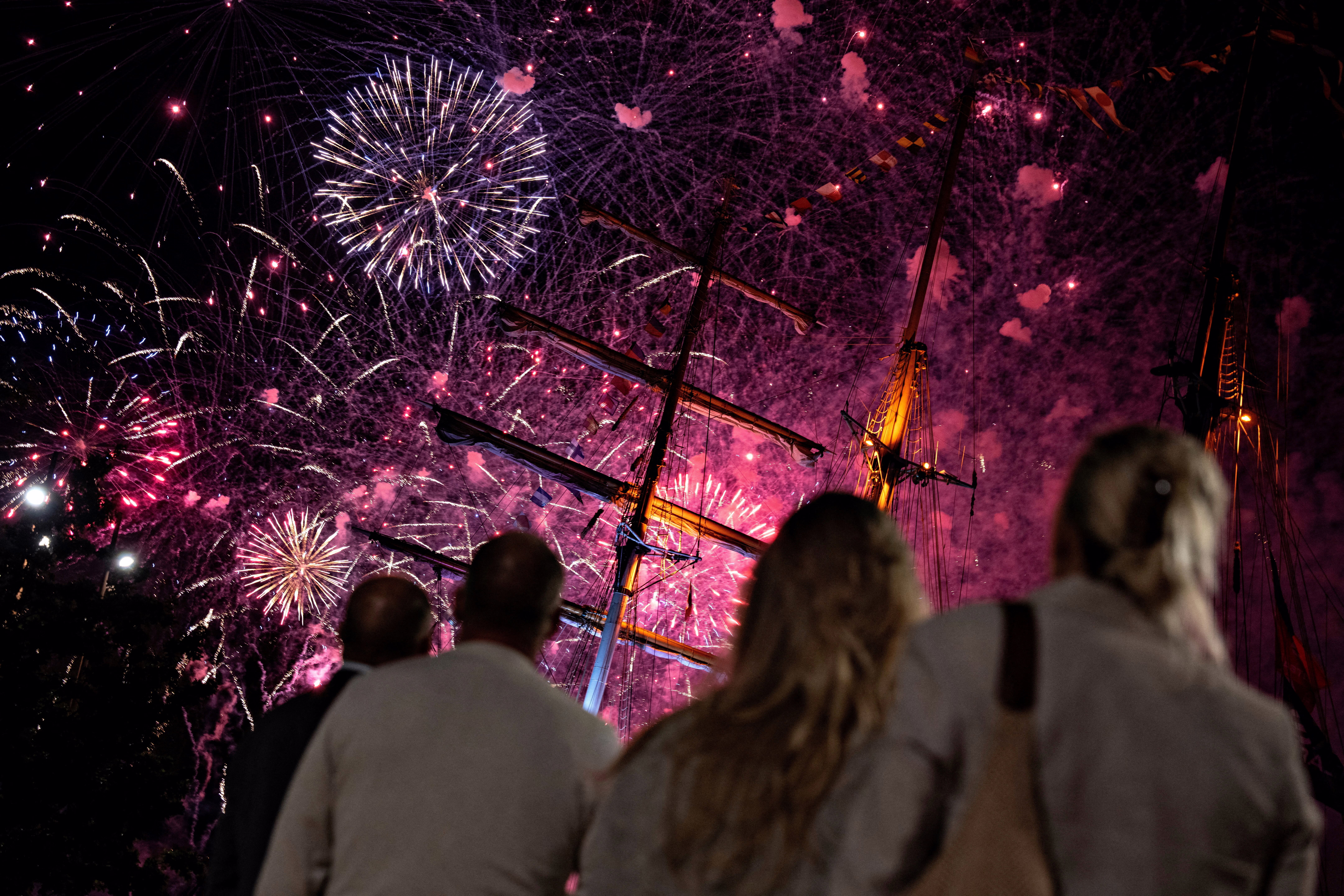 People watch fireworks explode above tall ships.