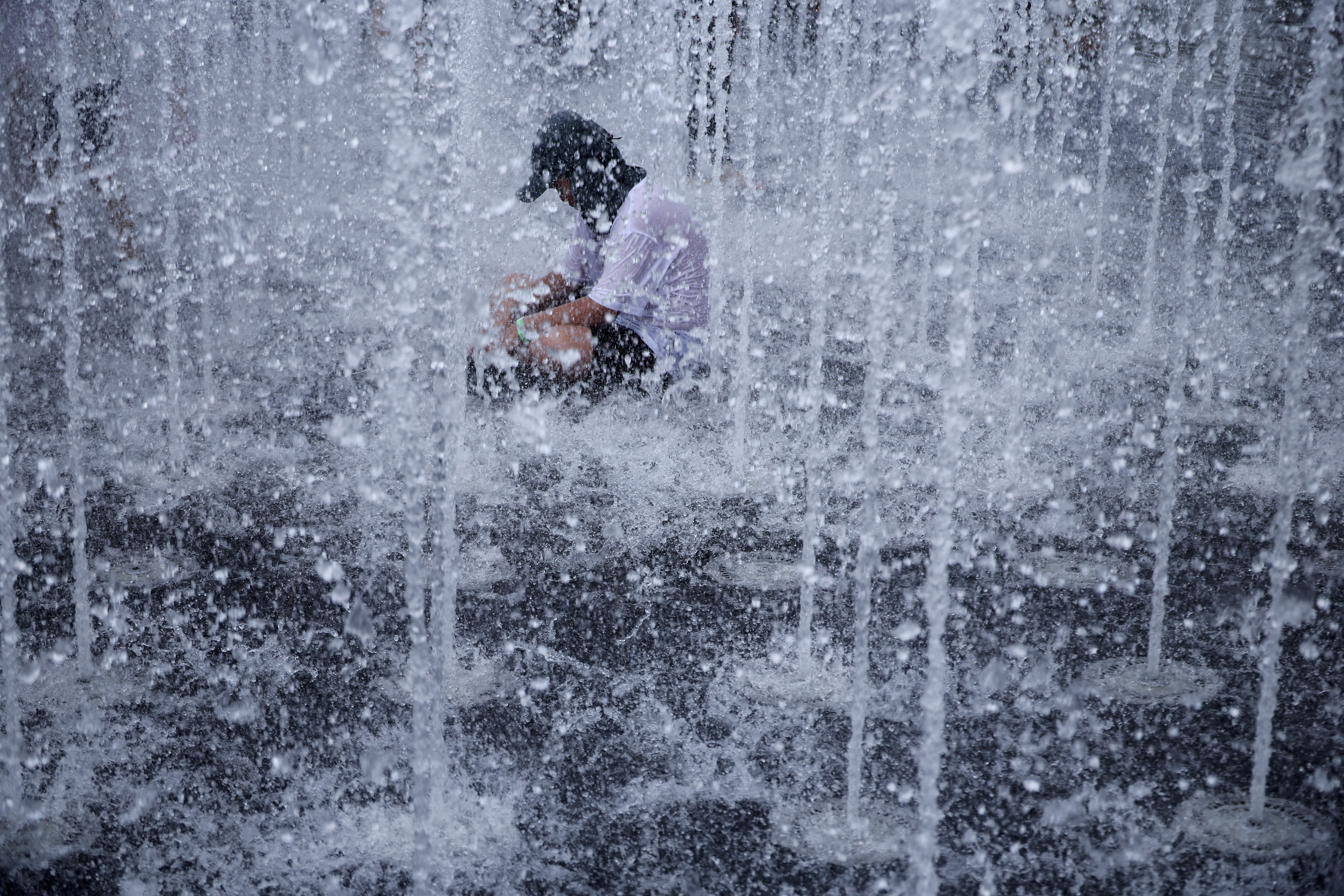 A boy cools down in a fountain, surrounded by jets of water.