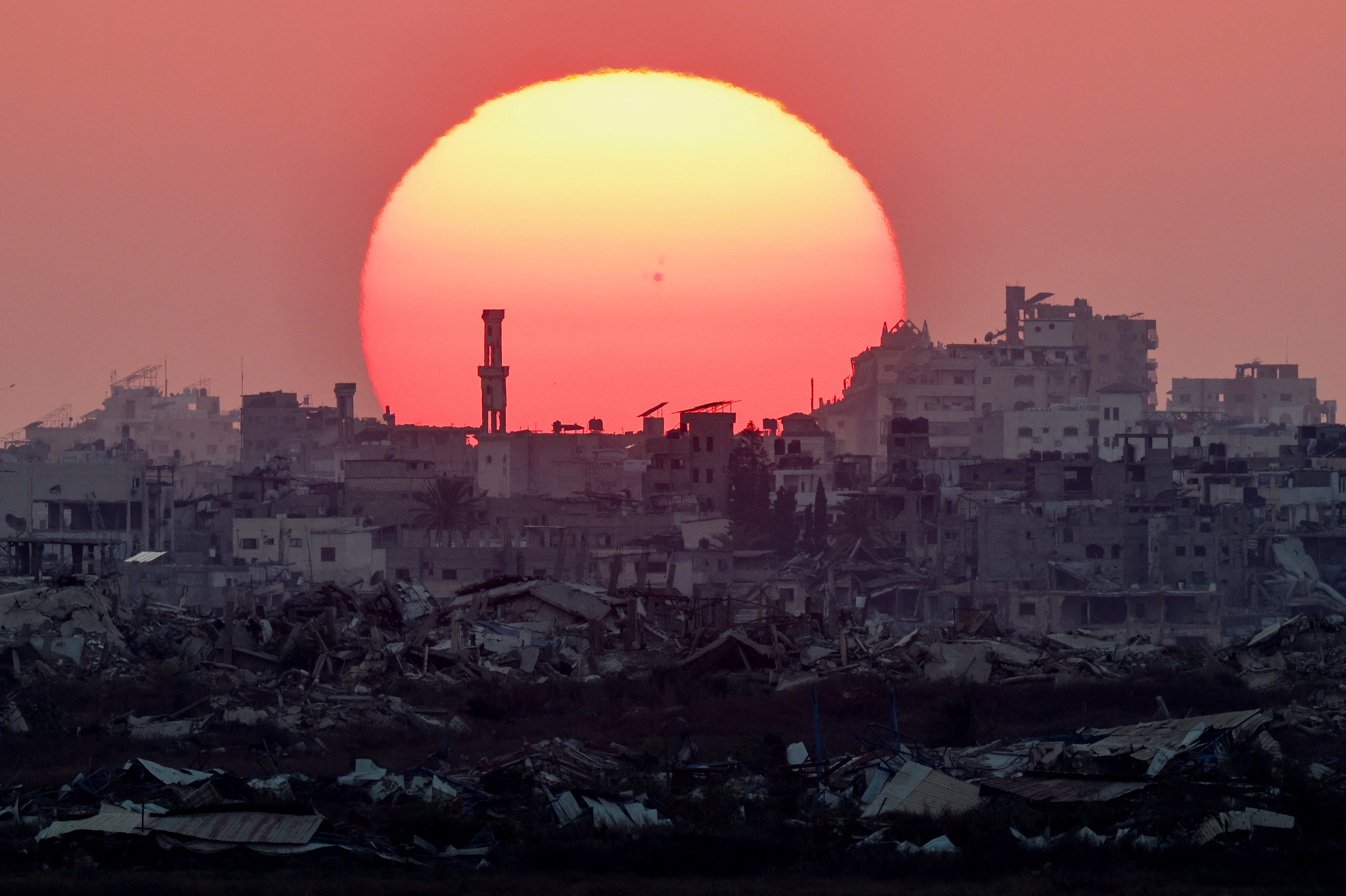 The sun sets over Gaza, with many damaged or destroyed buildings visible.
