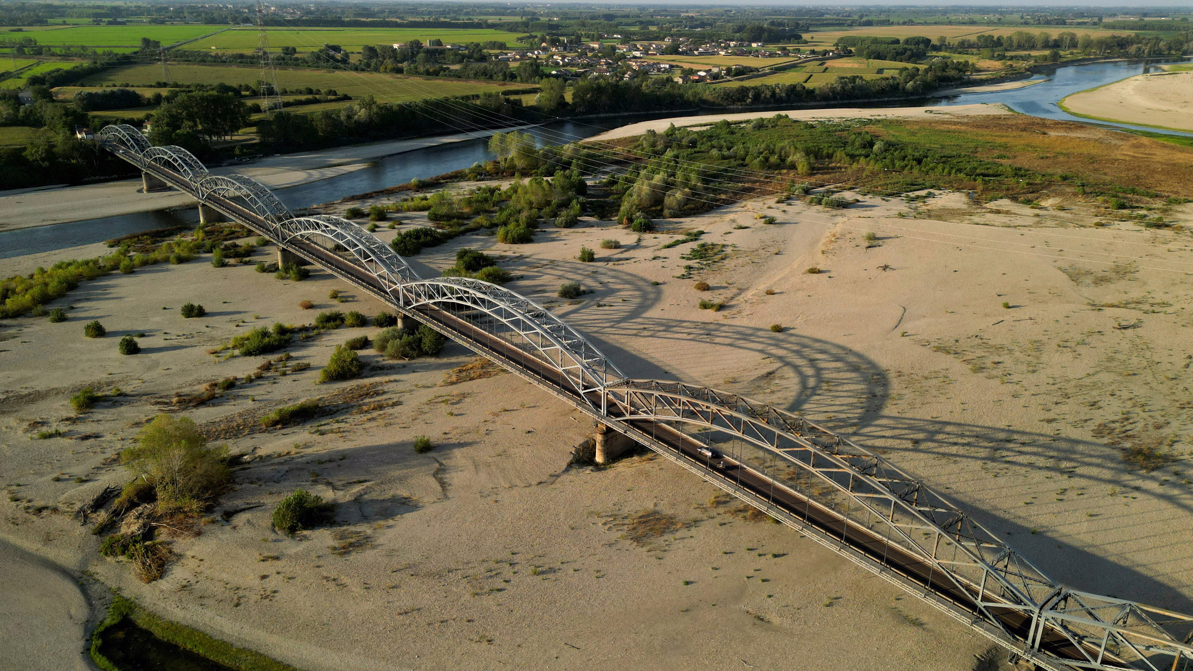 A drone view shows a river running low under a road bridge.