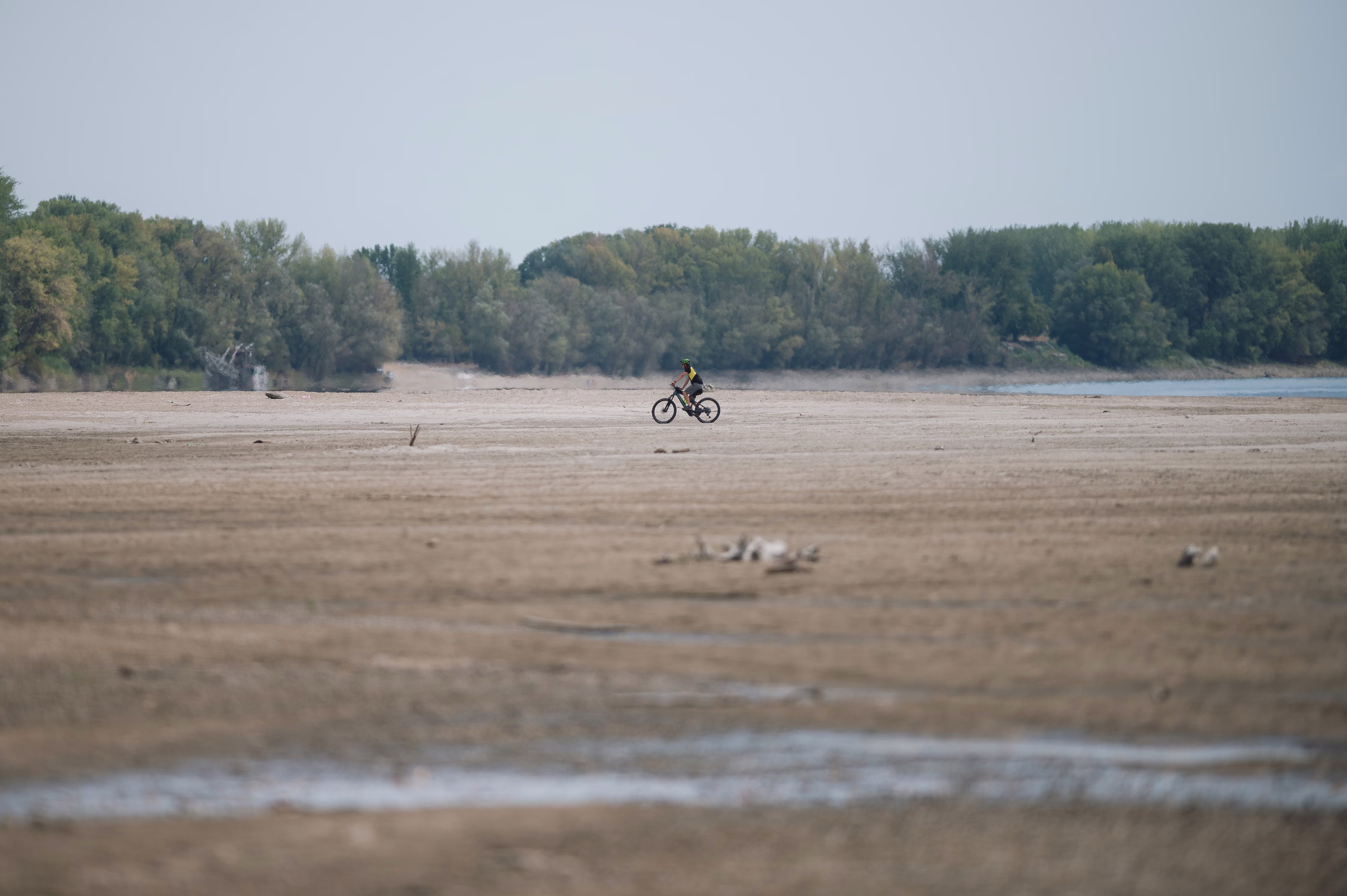 A cyclist rides across a dry riverbed.