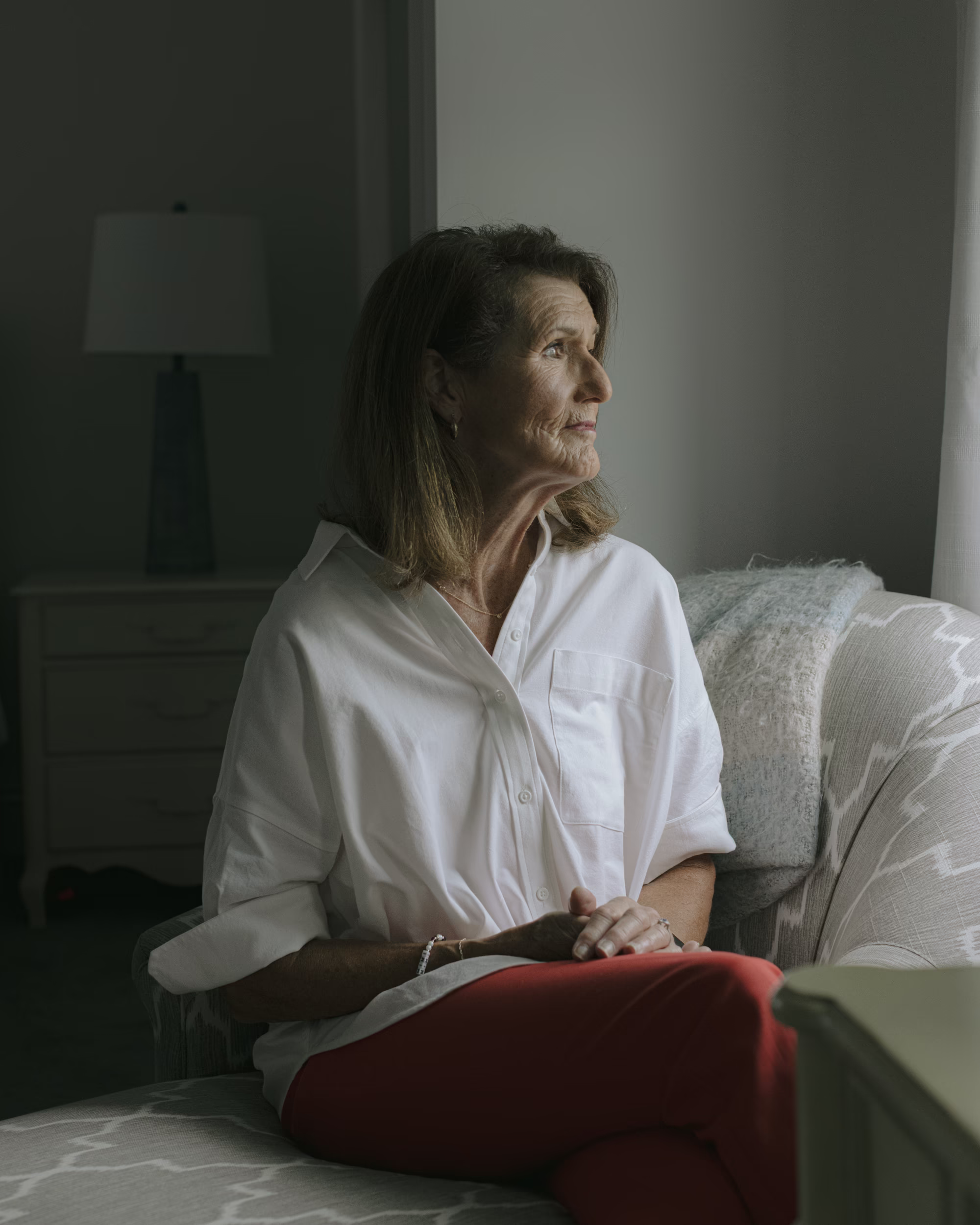 photo of woman in profile wearing white button-down shirt and red pants, sitting on sofa