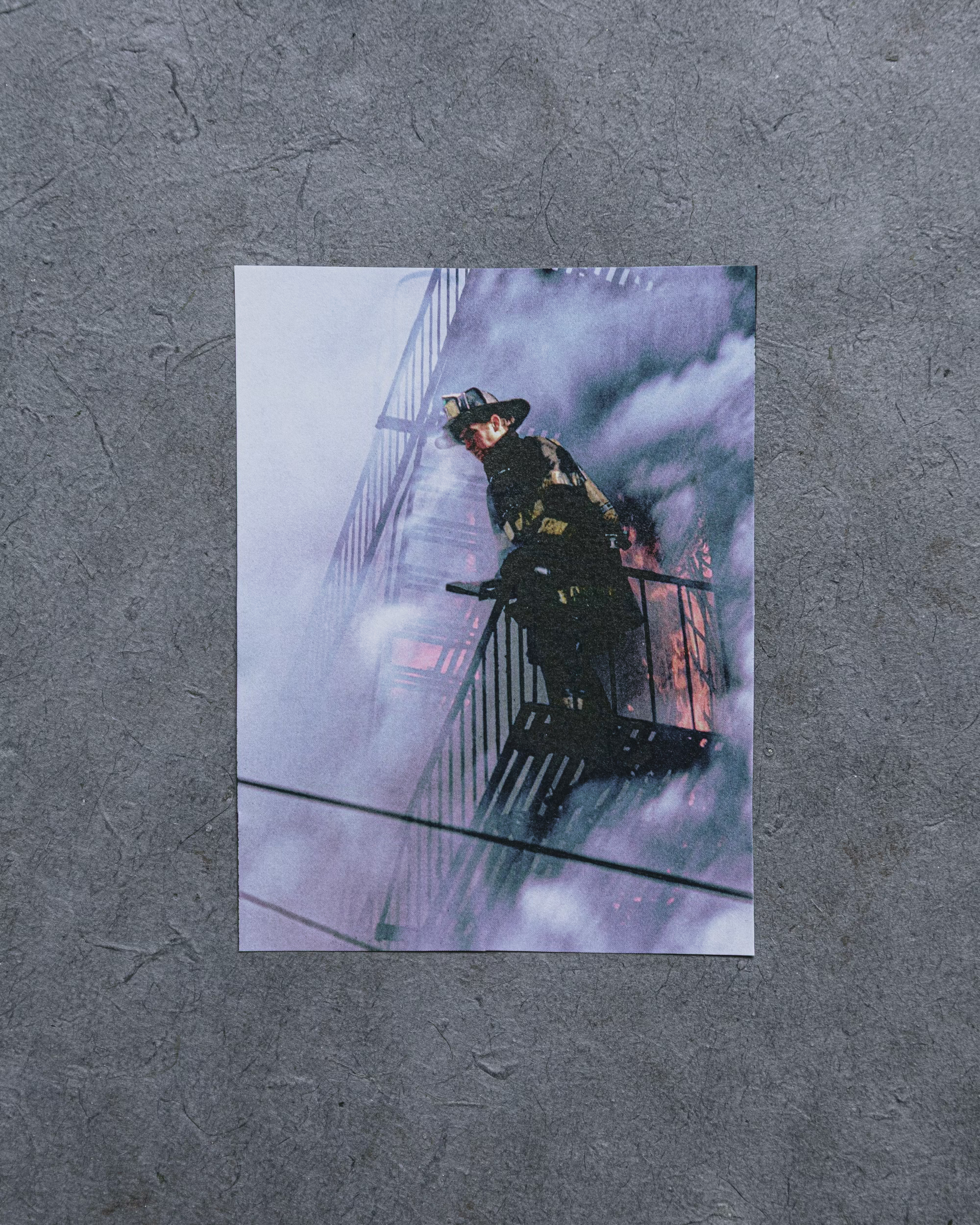 photo of firefighter standing on fire escape of burning building with flames and smoke behind