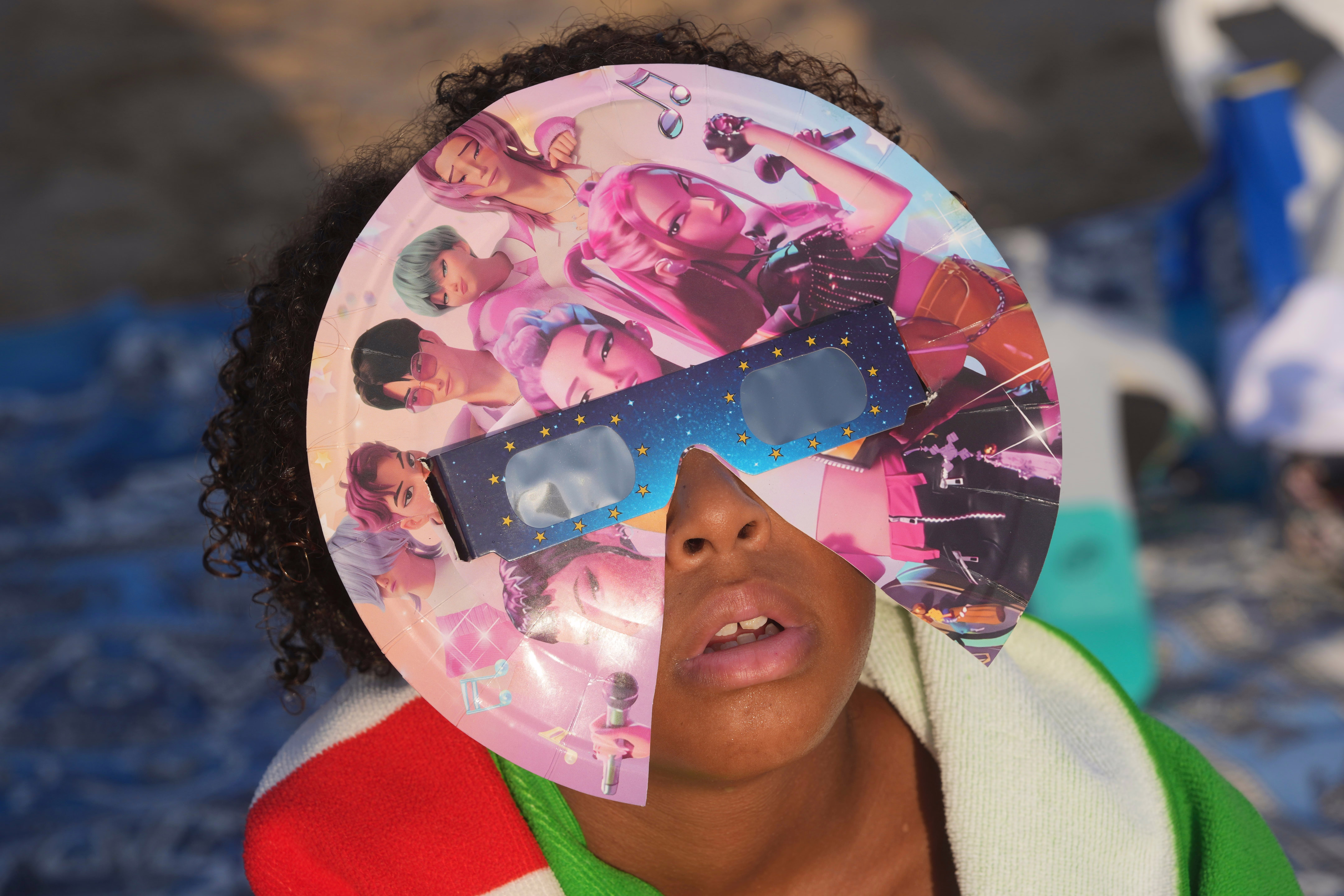 A young person wears special eclipse glasses decorated with 'K-Pop Demon Hunters' characters.