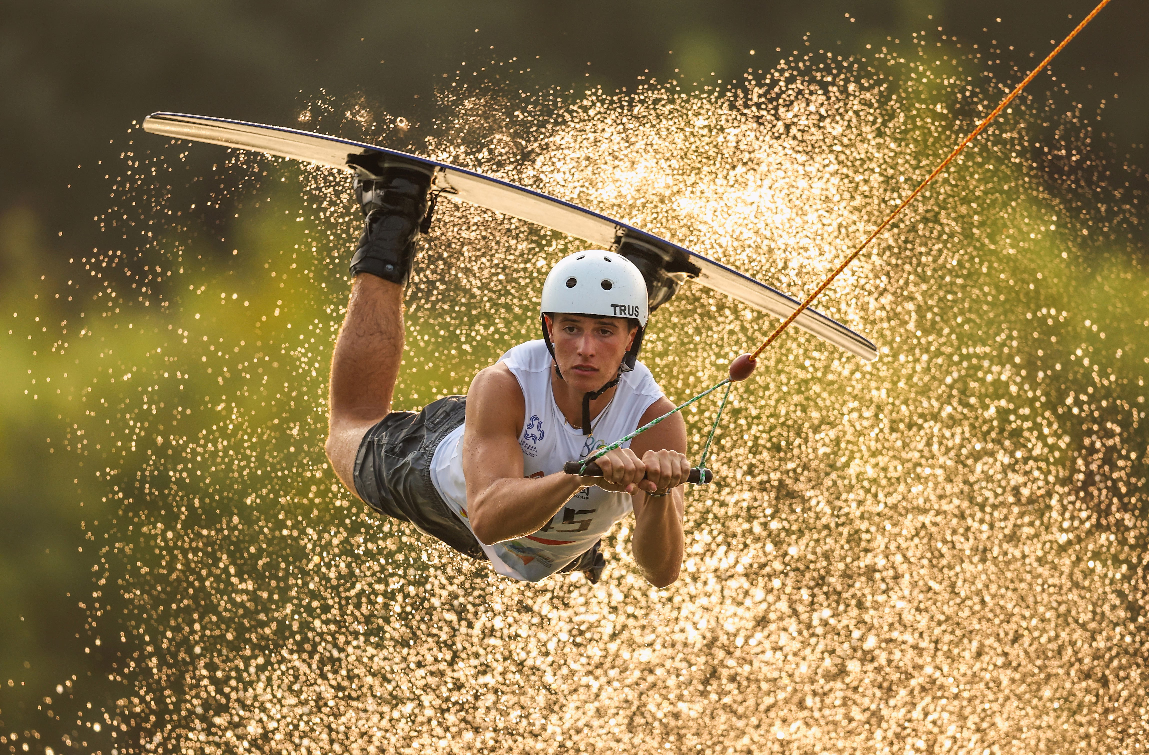 A wakeboarder holds onto a tow rope as they take a jump, kicking up a spray of water.