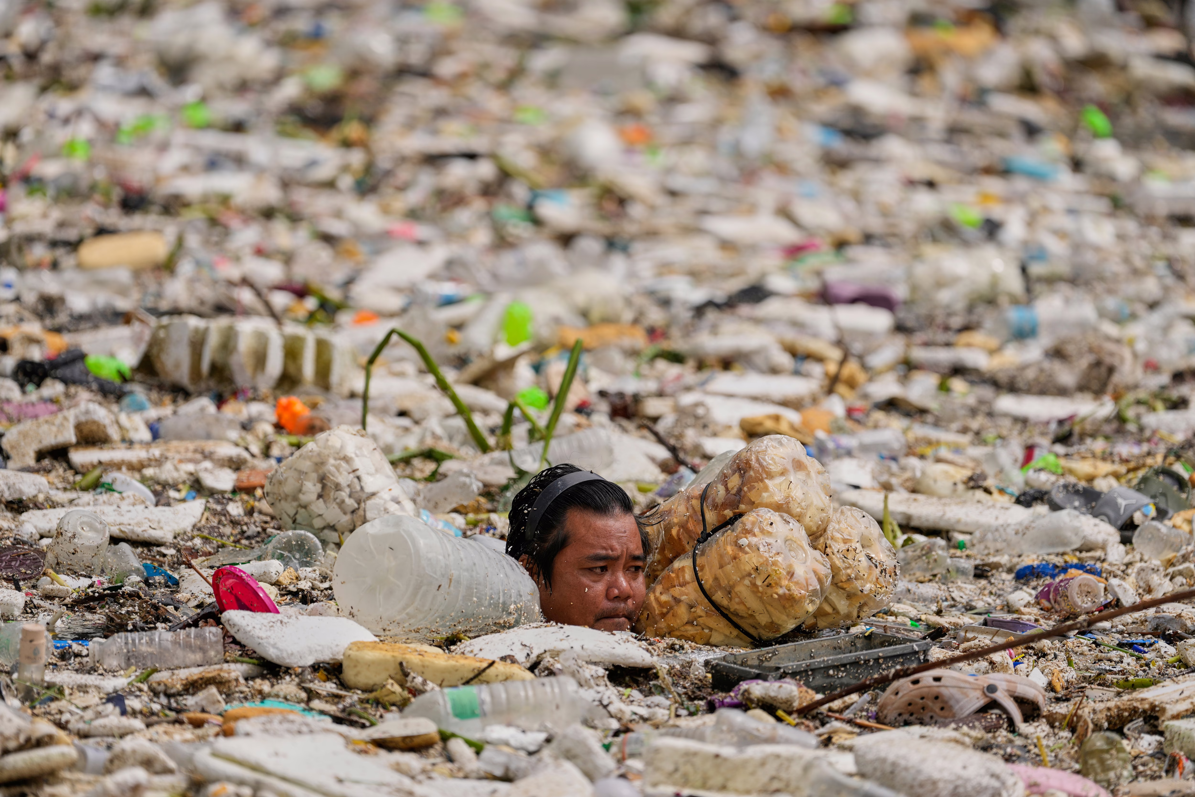 A person works to clear floating garbage, only their head visible among a sea of debris.