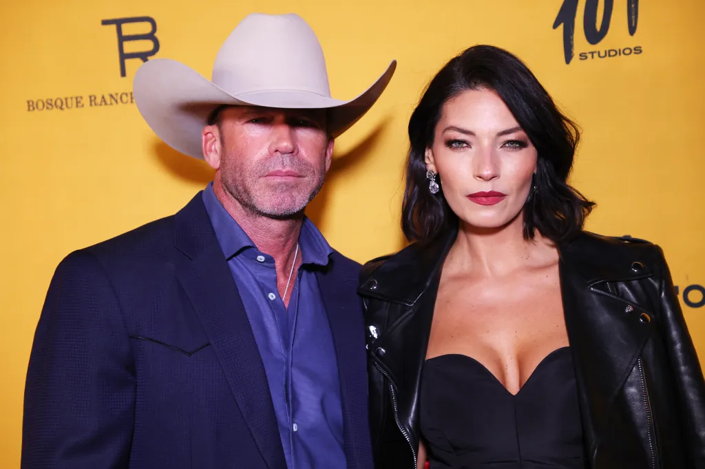 Taylor Sheridan wearing a cowboy hat and a blue suit, and Nicole Sheridan wearing a black leather jacket and red lipstick, at the premiere for Paramount Network's 