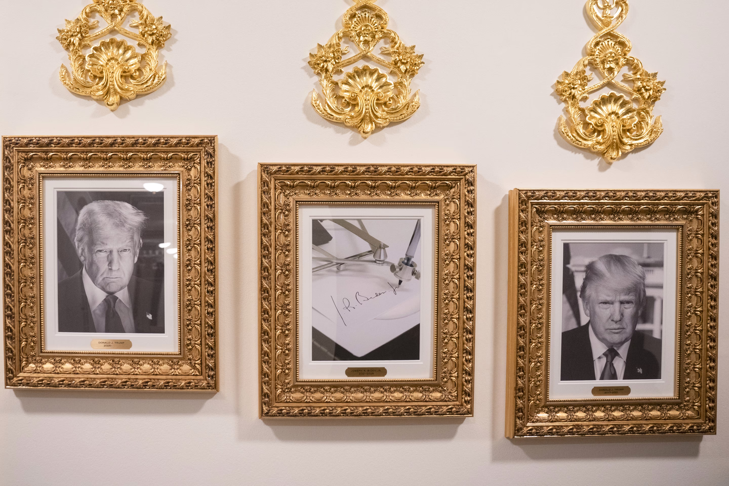 Two black and white photos of Donald Trump and in the middle is Biden's signature, all in gold frames