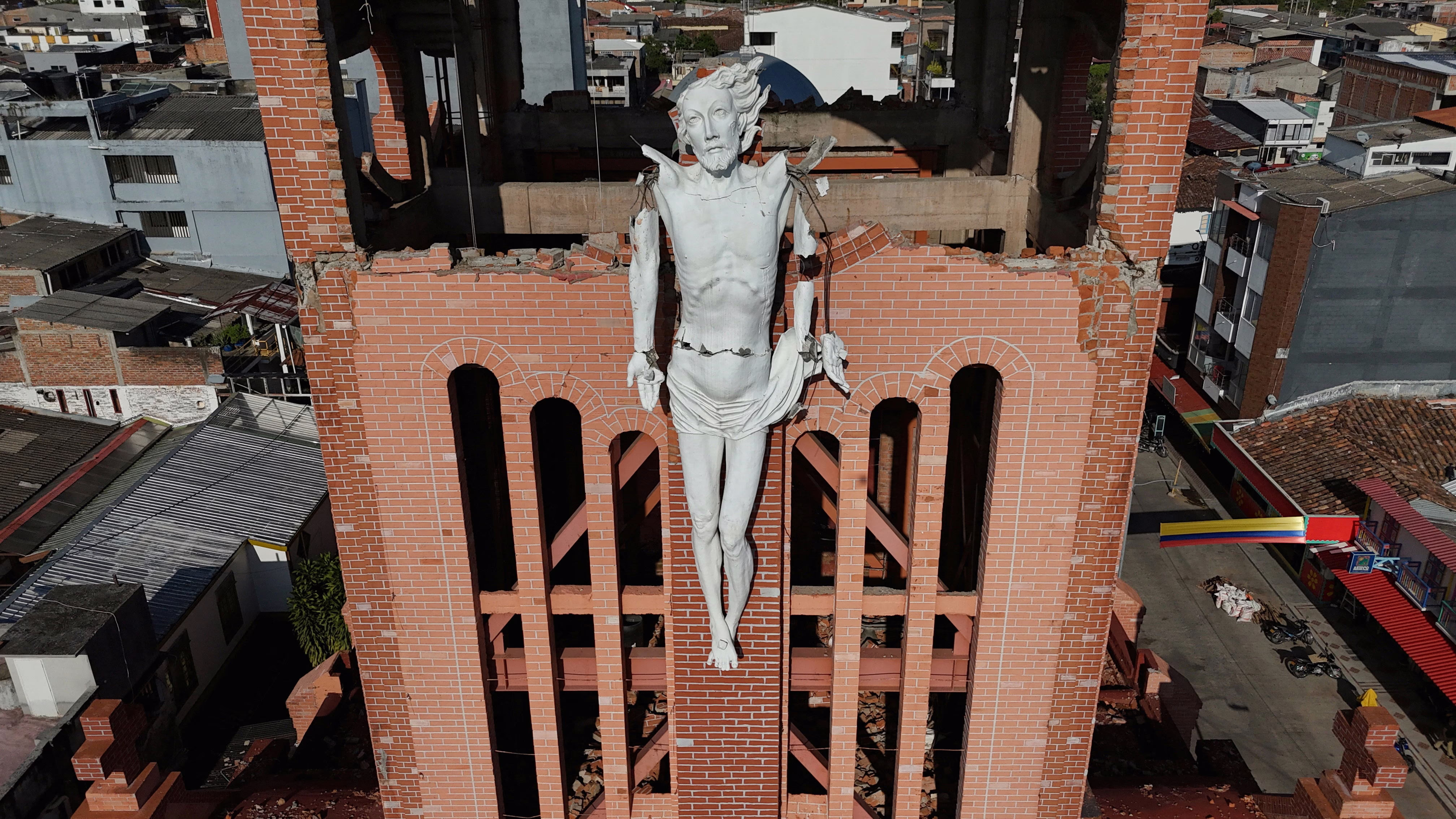 A drone view of a quake-damaged church tower with a fractured statue of Christ on the outside wall