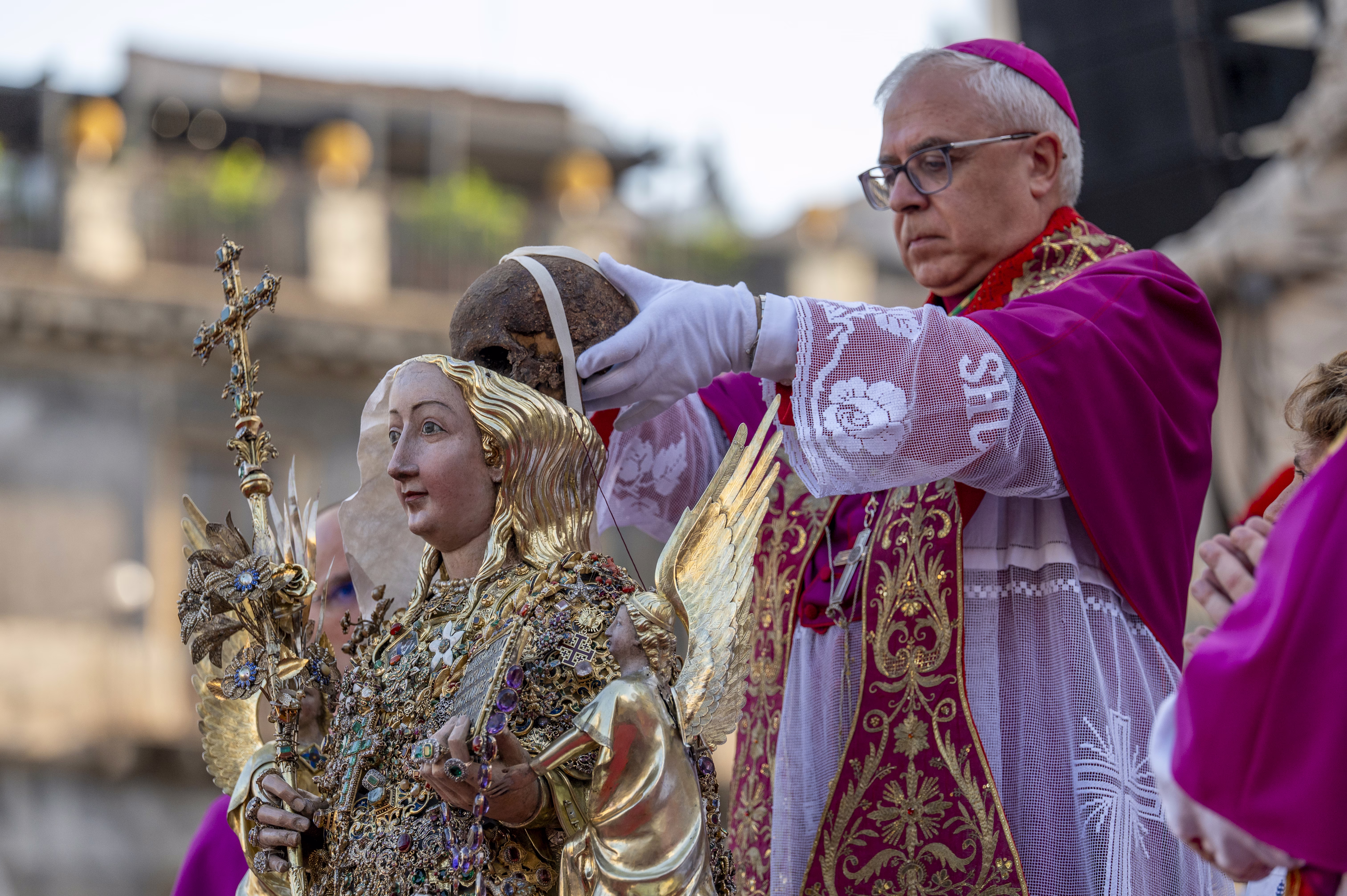 An Archbishop places the skull of a saint inside the head of ornate reliquary bust. 