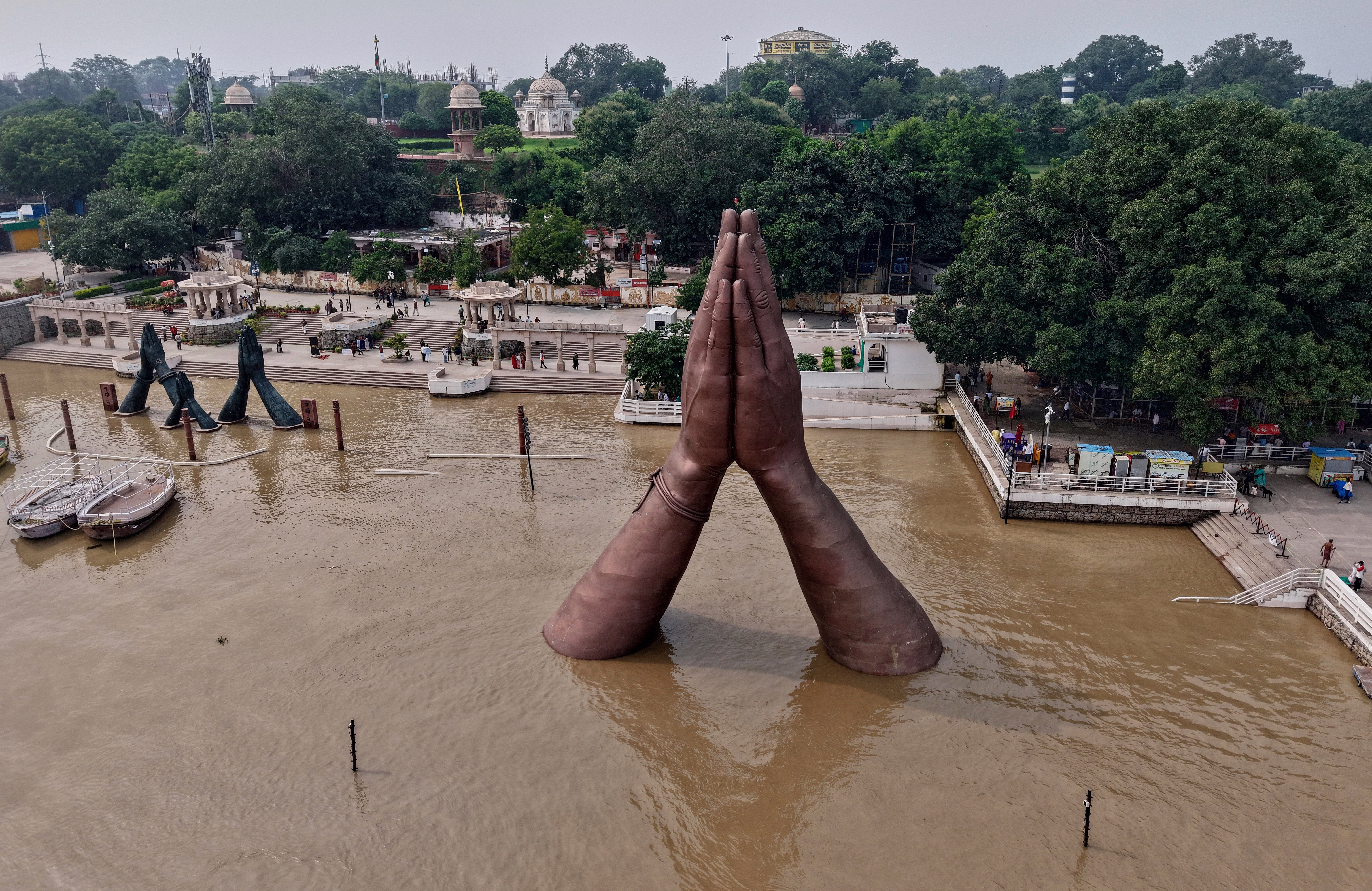 A large sculpture of praying hands, situated just offshore of a riverbank, during a high-water event.