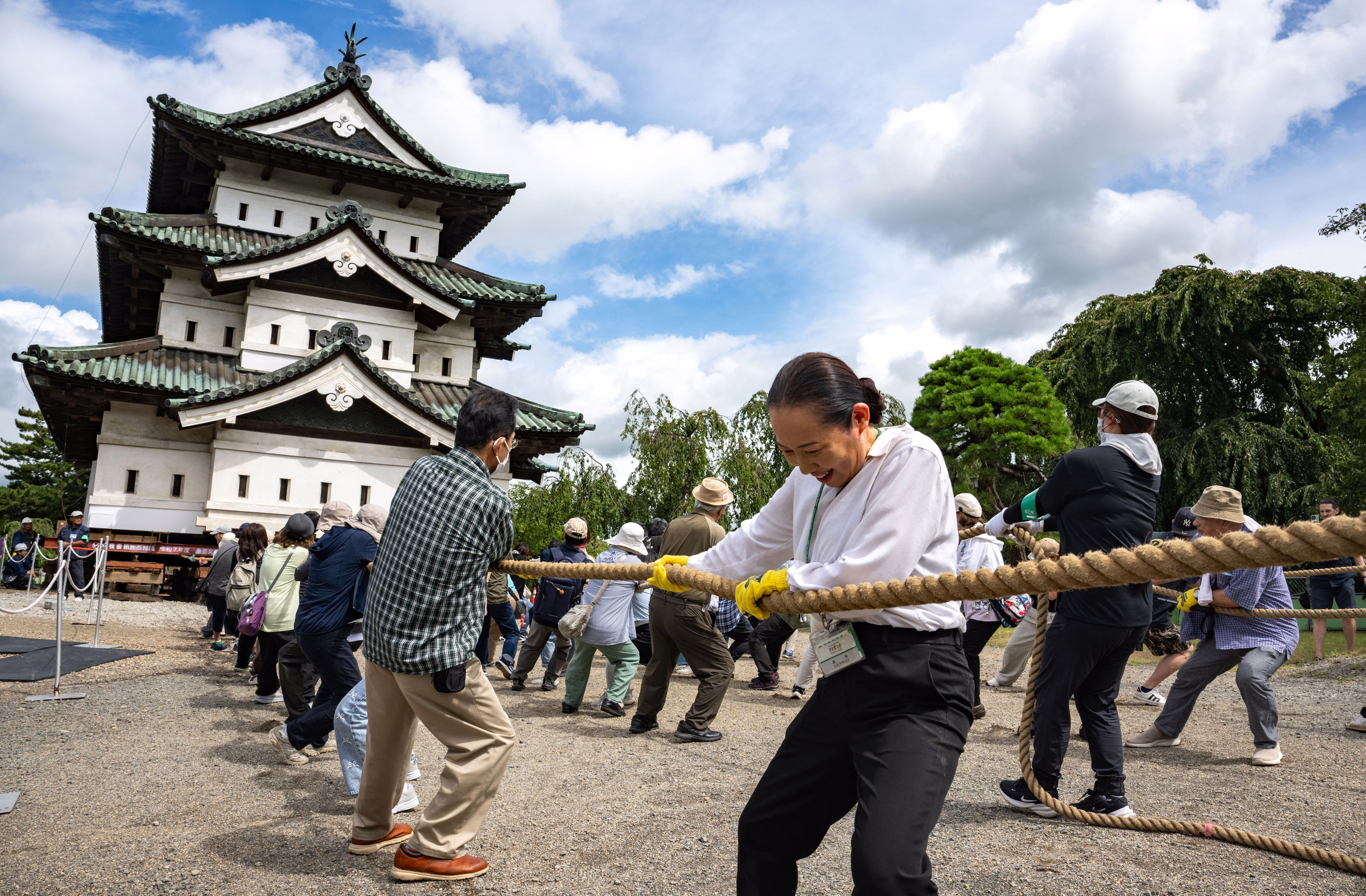 Civilians tug on large ropes, pulling a castle that has been raised up for repairs.