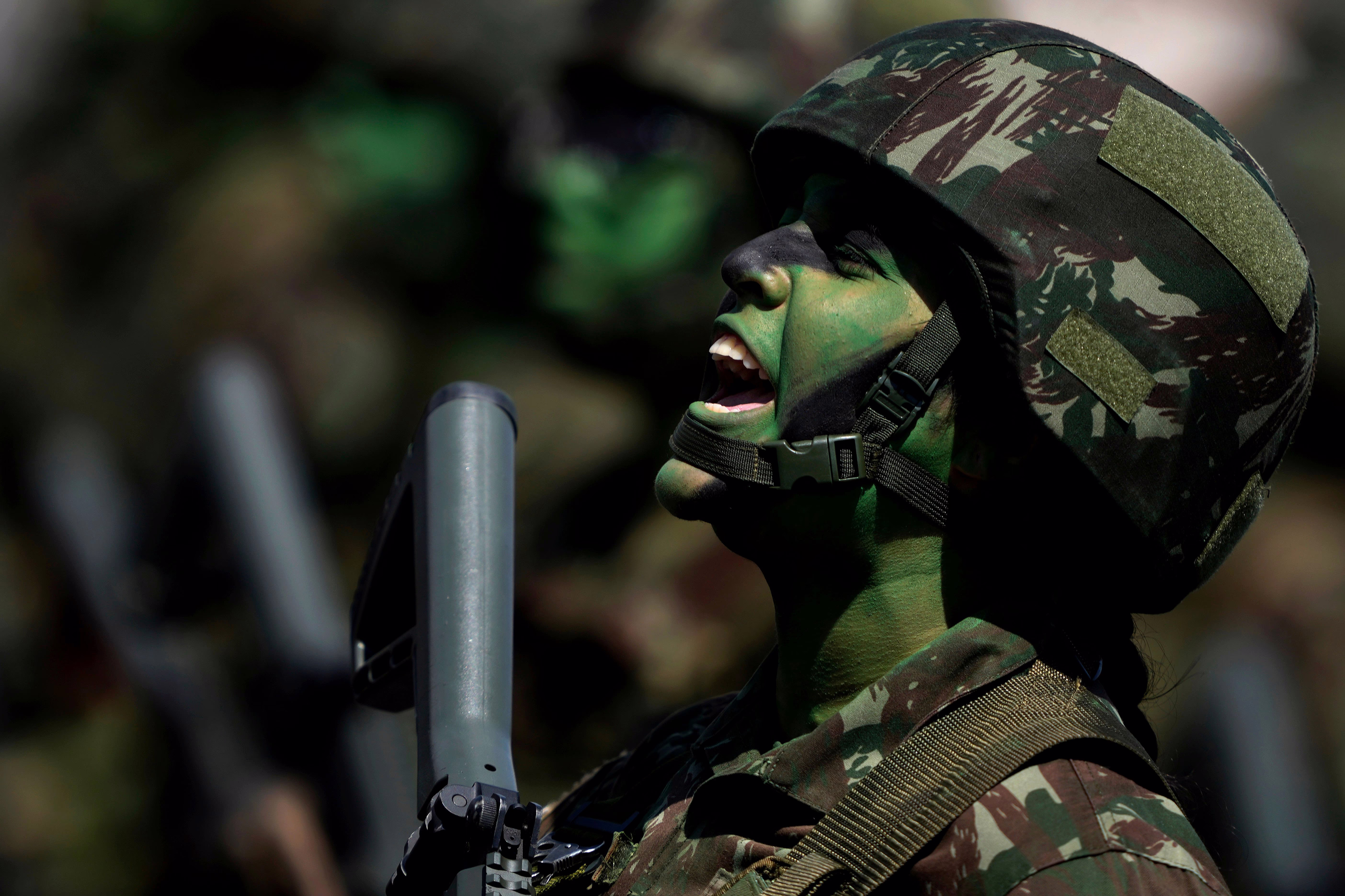 A soldier, wearing camouflage makeup and uniform, sings during a parade.