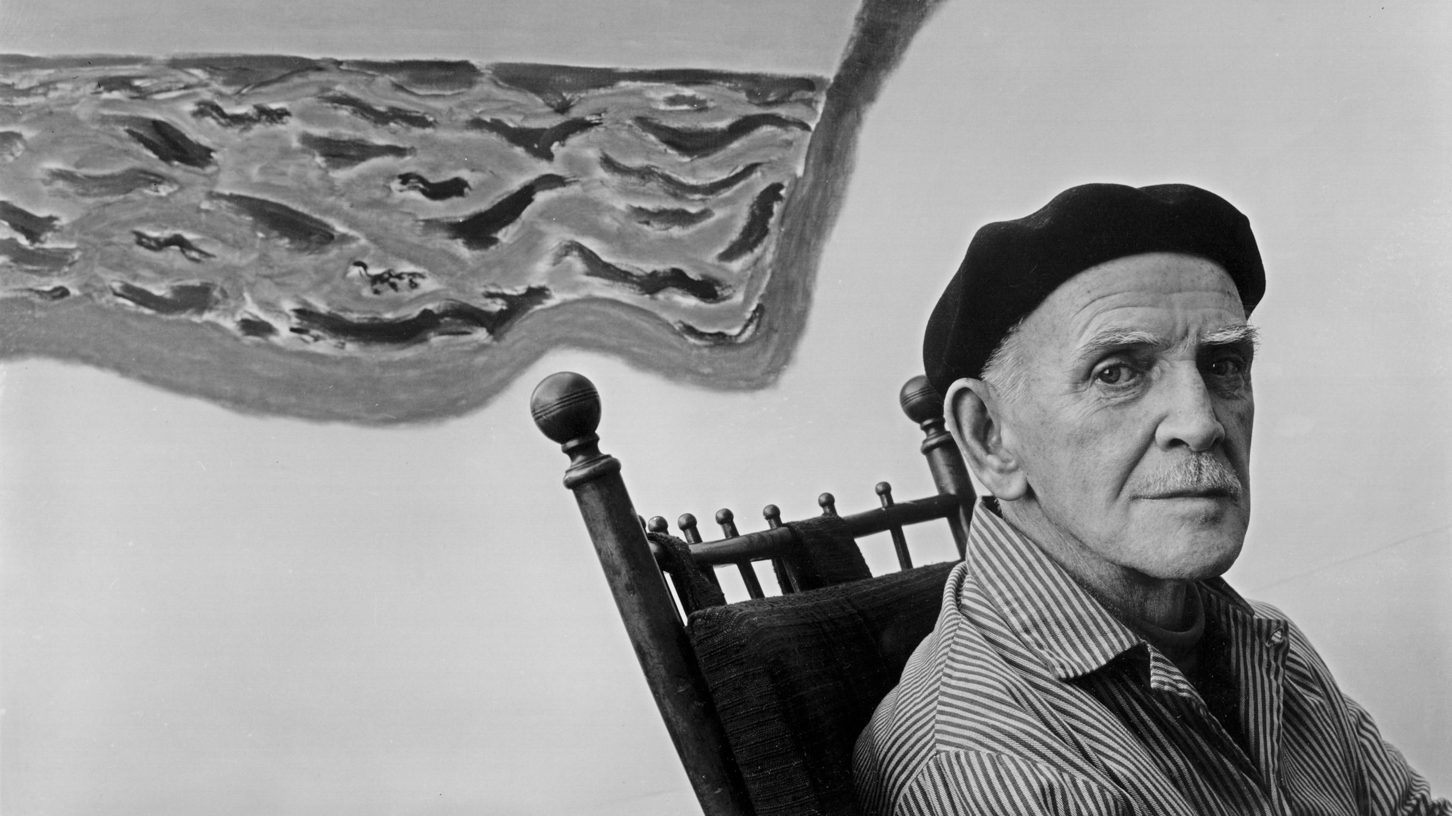 A man sits in a chair in front of a painting.