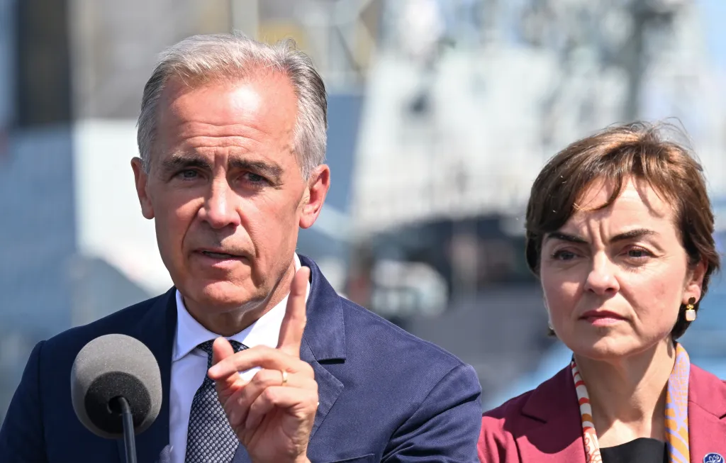 Canadian Prime Minister Mark Carney speaks into a microphone, with Quebec Premier Christine Frechette looking on.