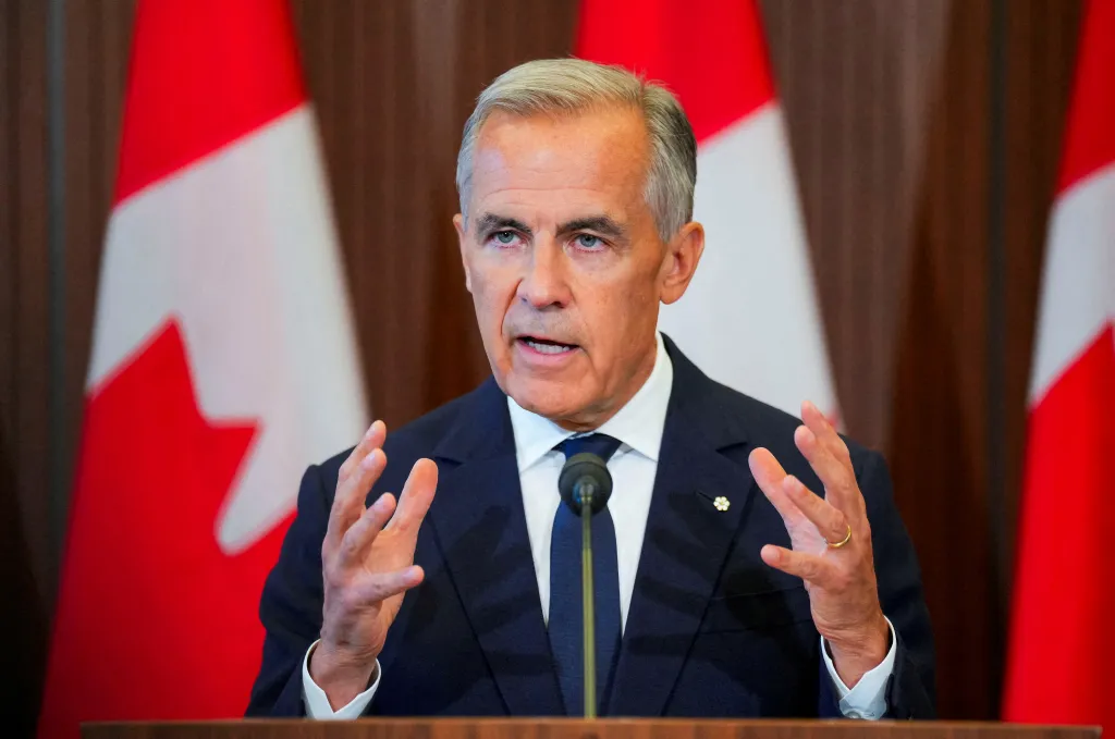 Canada's Prime Minister Mark Carney speaking at a news conference with Canadian flags in the background.