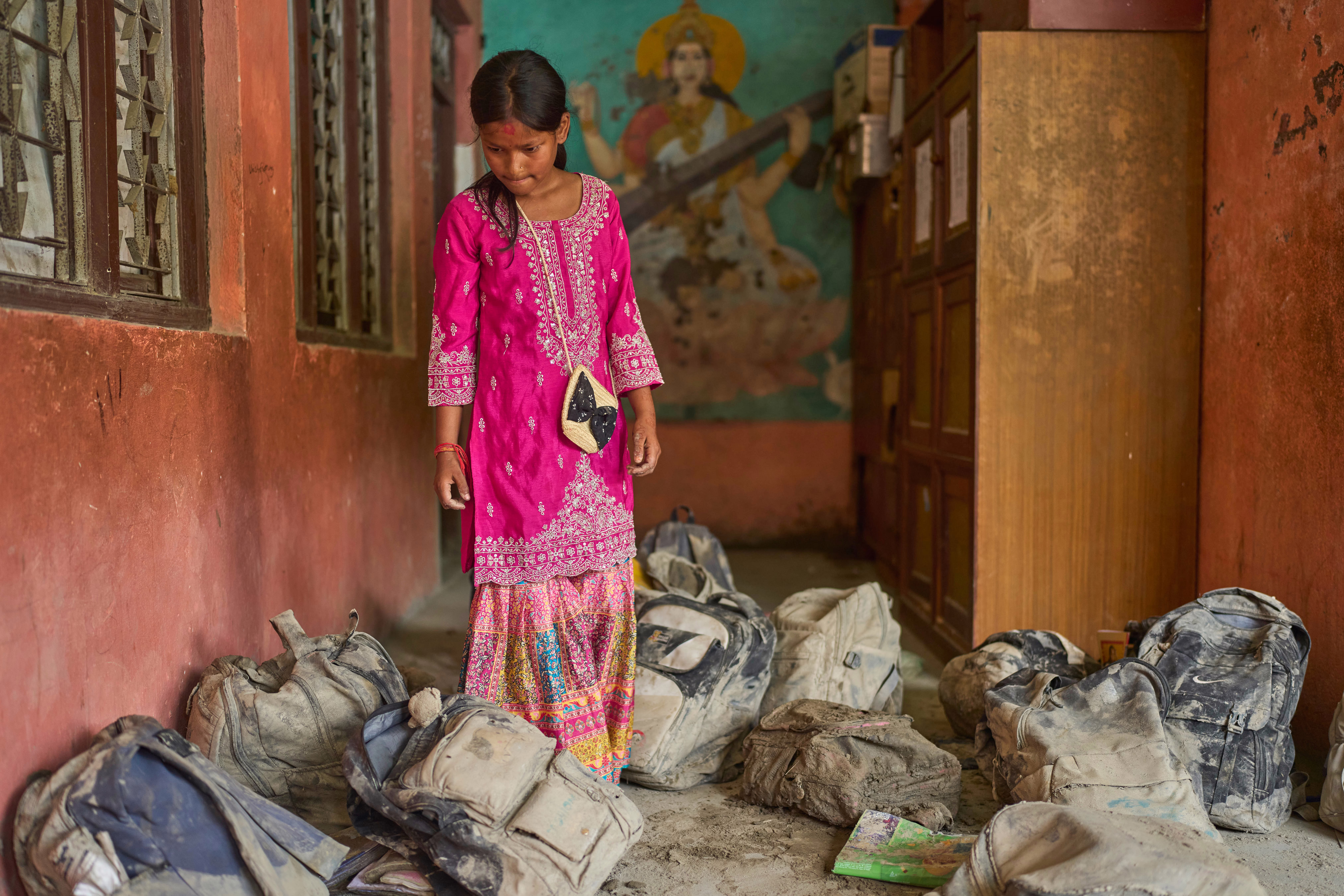 A student searches for her school bag in a pile of backpacks extracted from the mud after a flood.