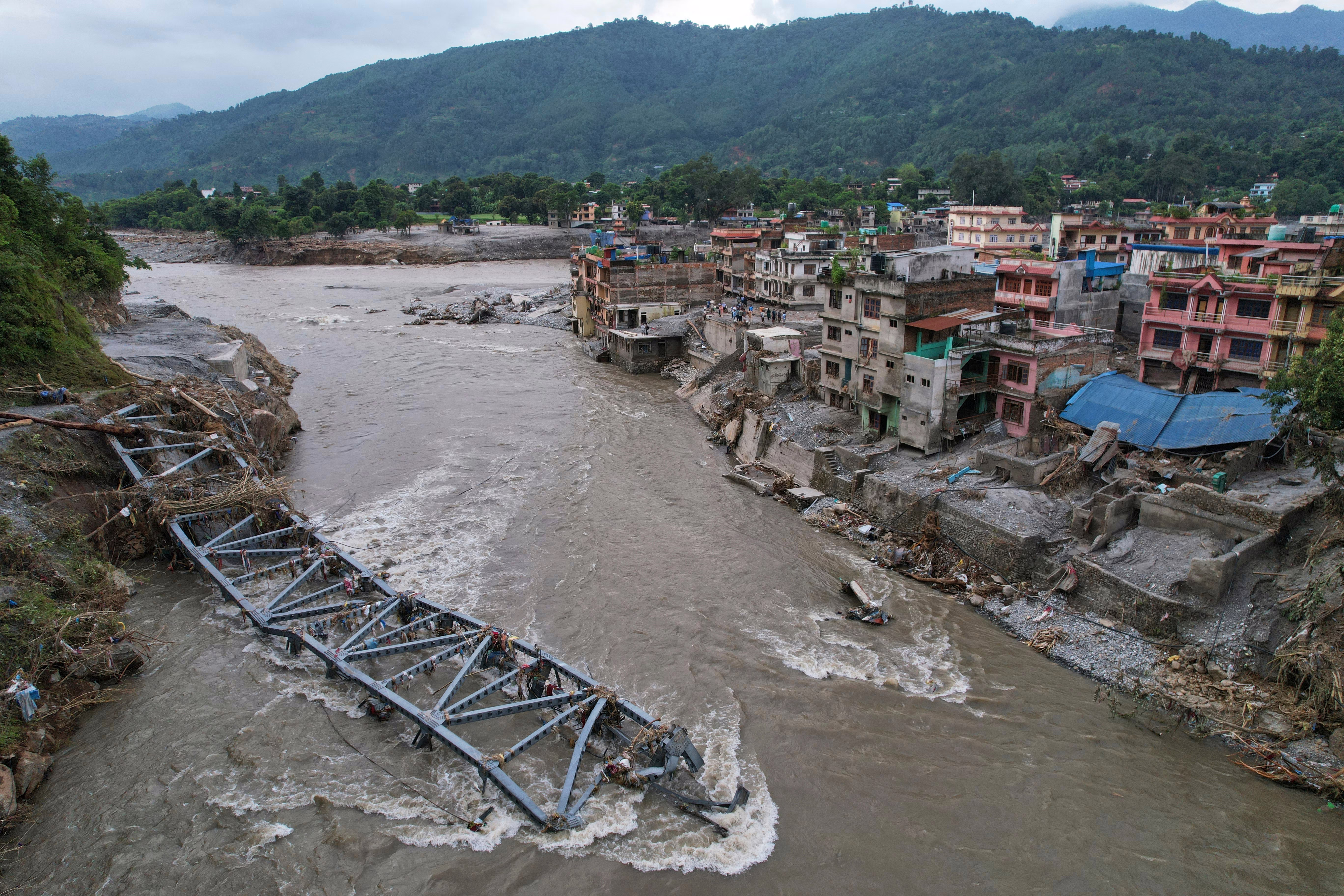 A drone view of a bridge toppled and damaged by flooding, still resting in a river