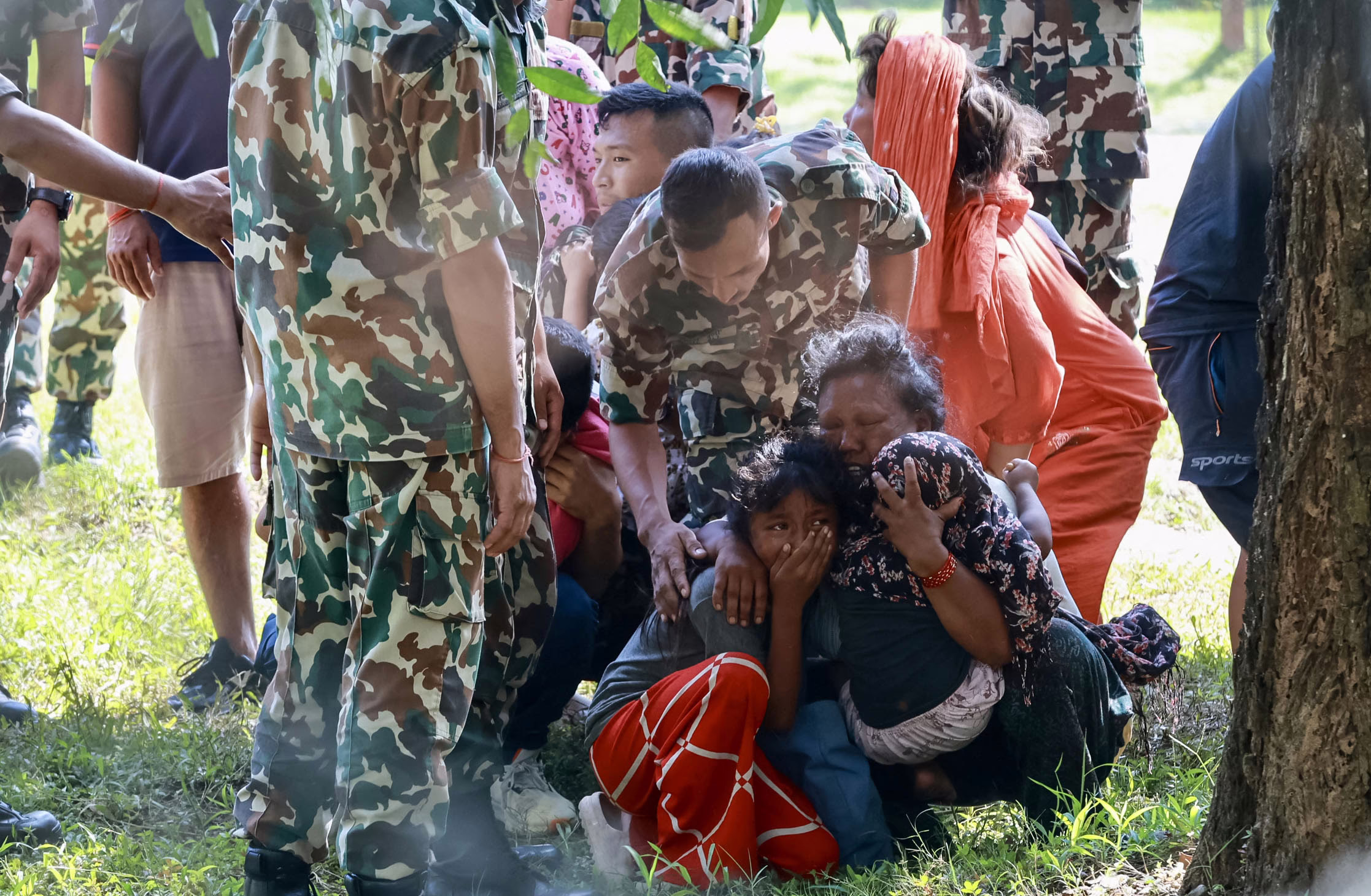 People react and embrace in a clearing, among soldiers and rescue workers.