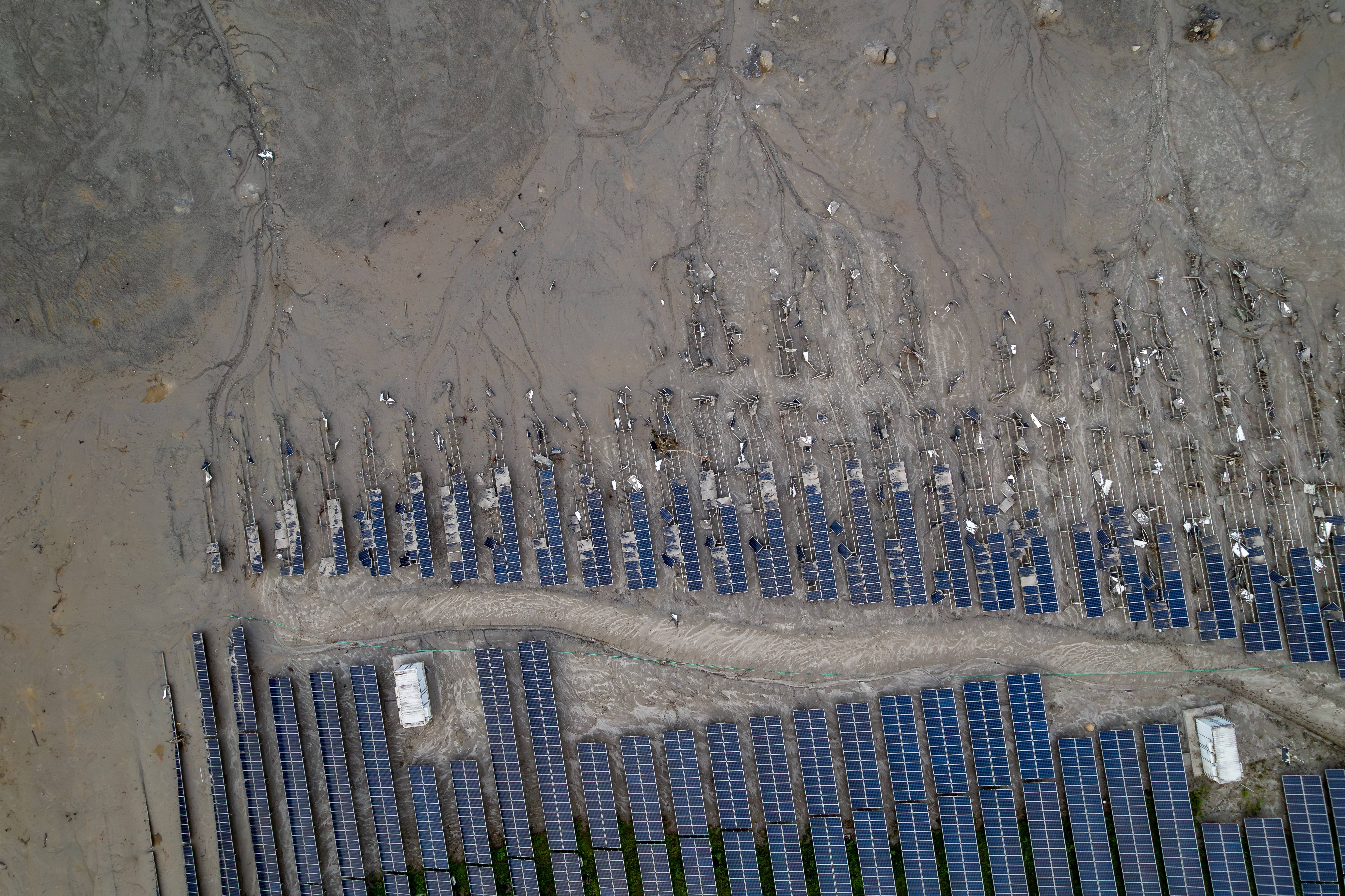 An aerial view of damaged and mud-covered solar panels along a flooded river