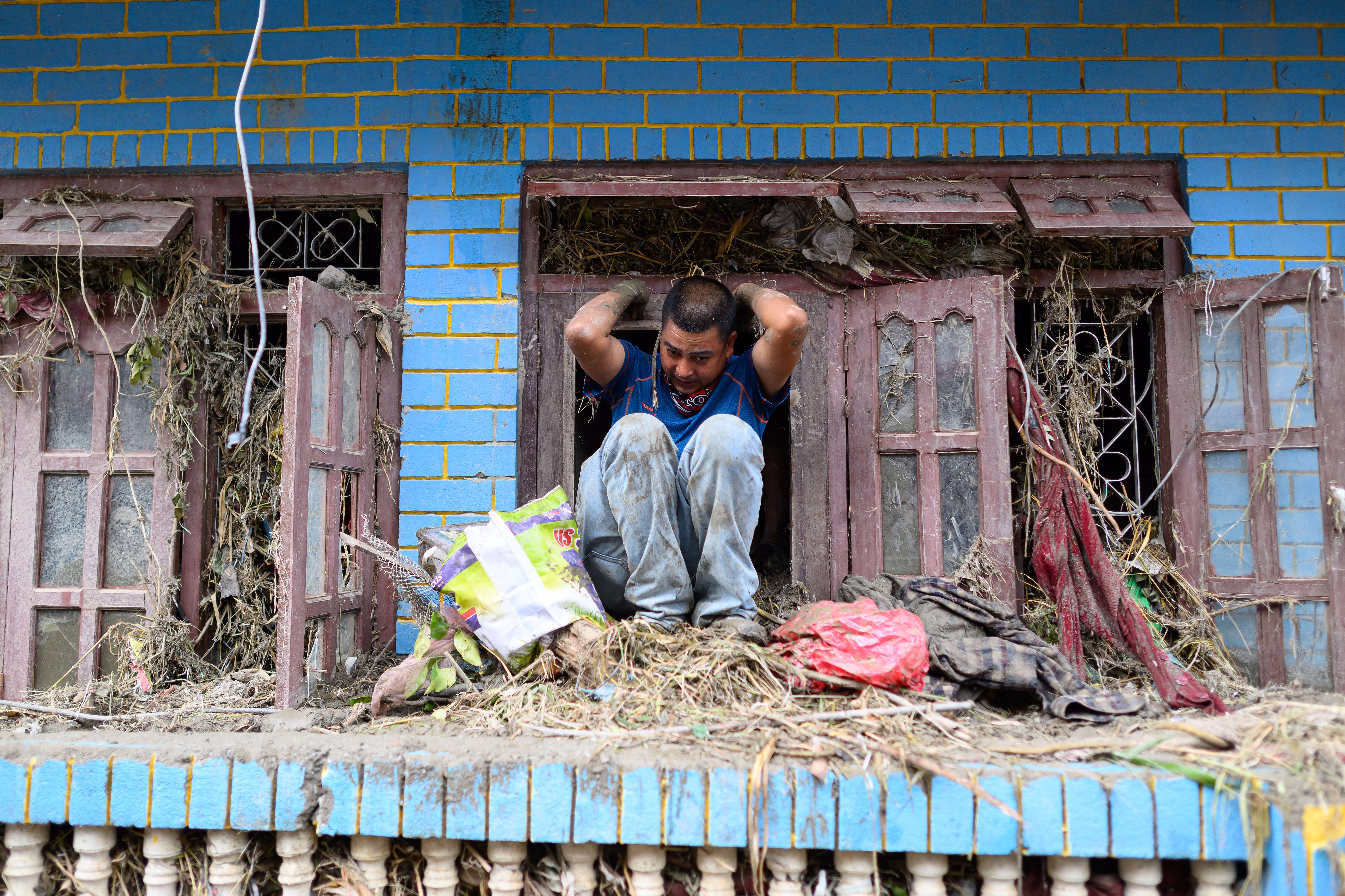 A man climbs out of a window after searching for his belongings inside his flood-damaged house.