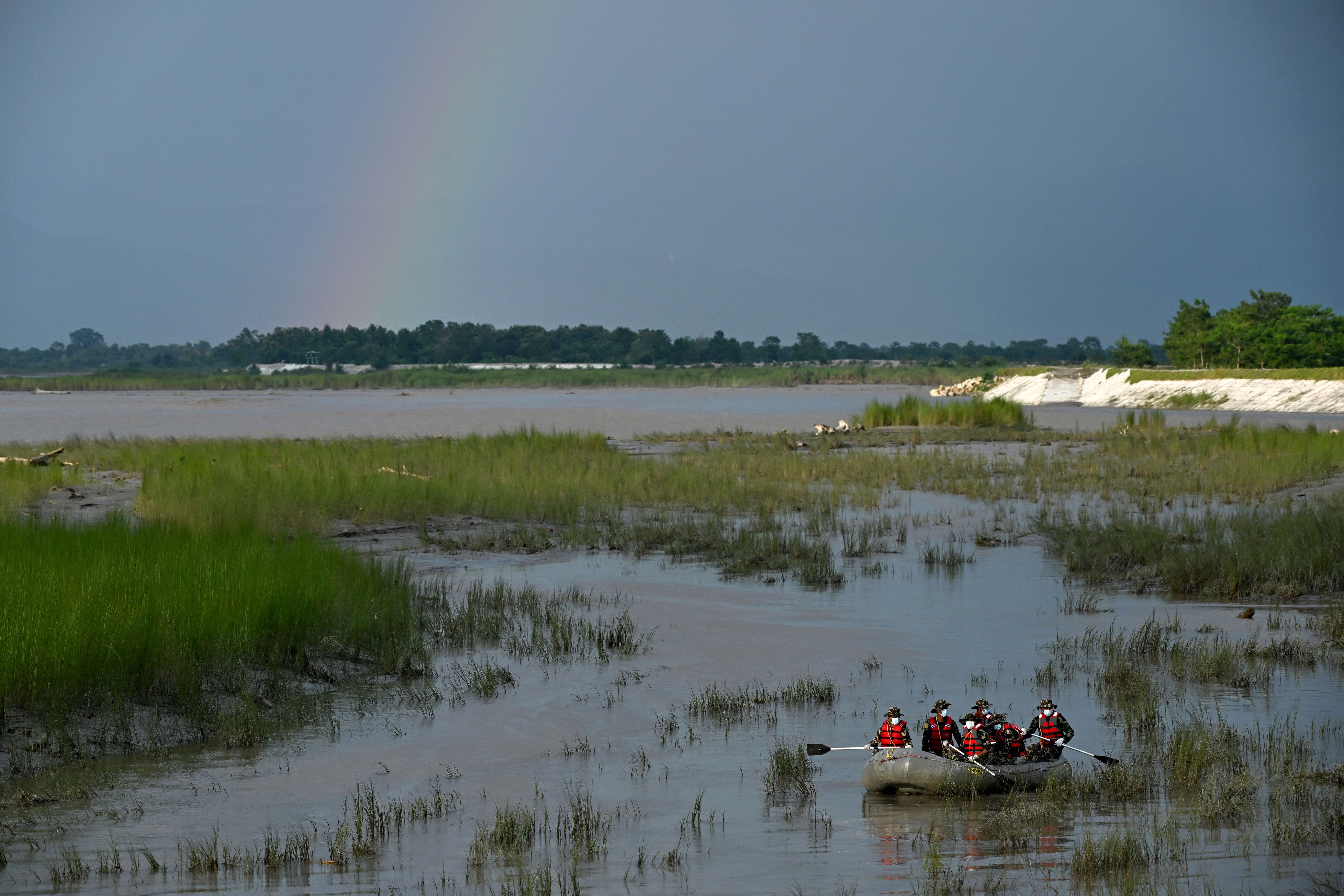 Several soldiers row an inflatable raft through river wetlands, searching for flood victims.