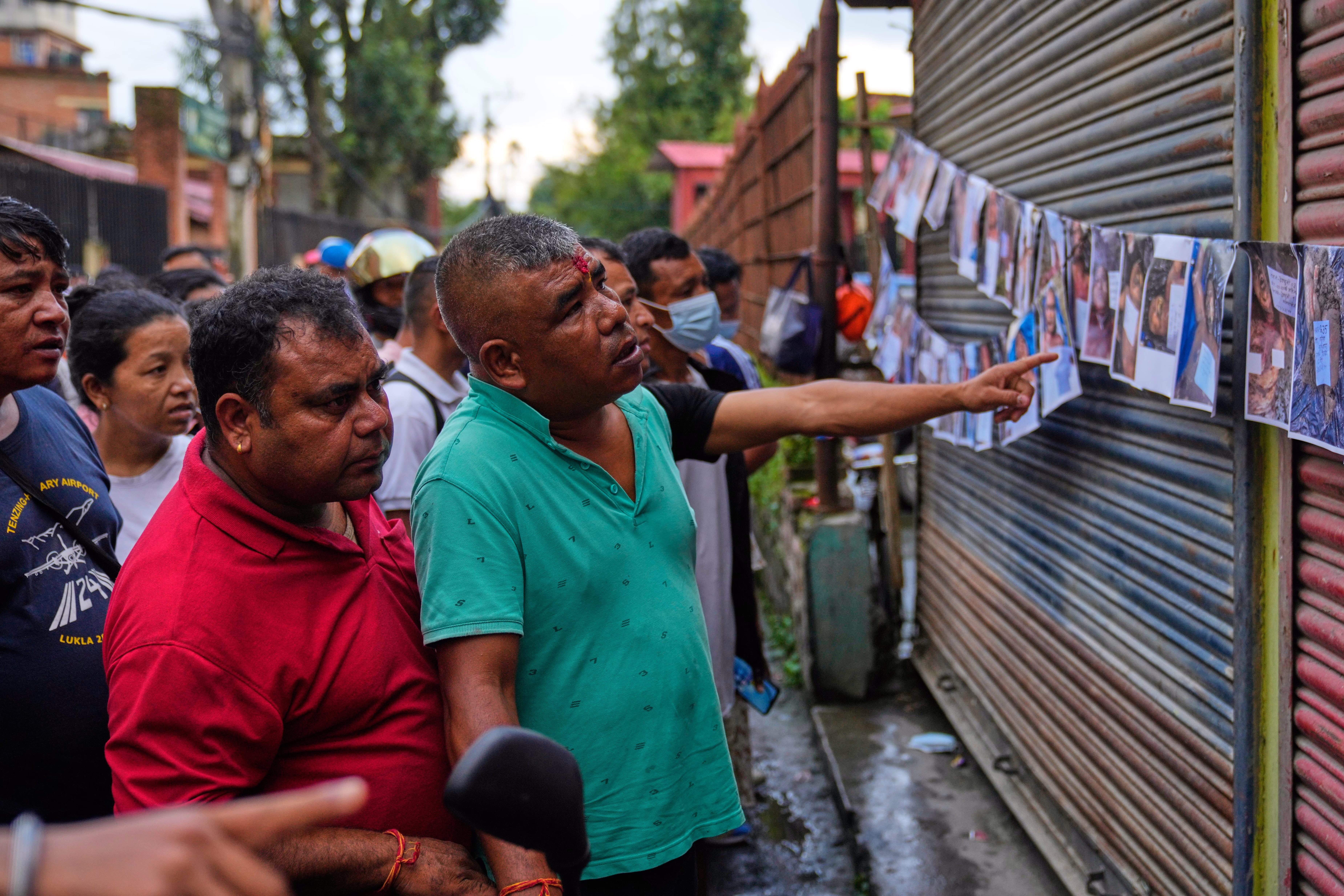 People look at photographs of unidentified flood victims displayed on a string tacked to a wall outside a hospital.