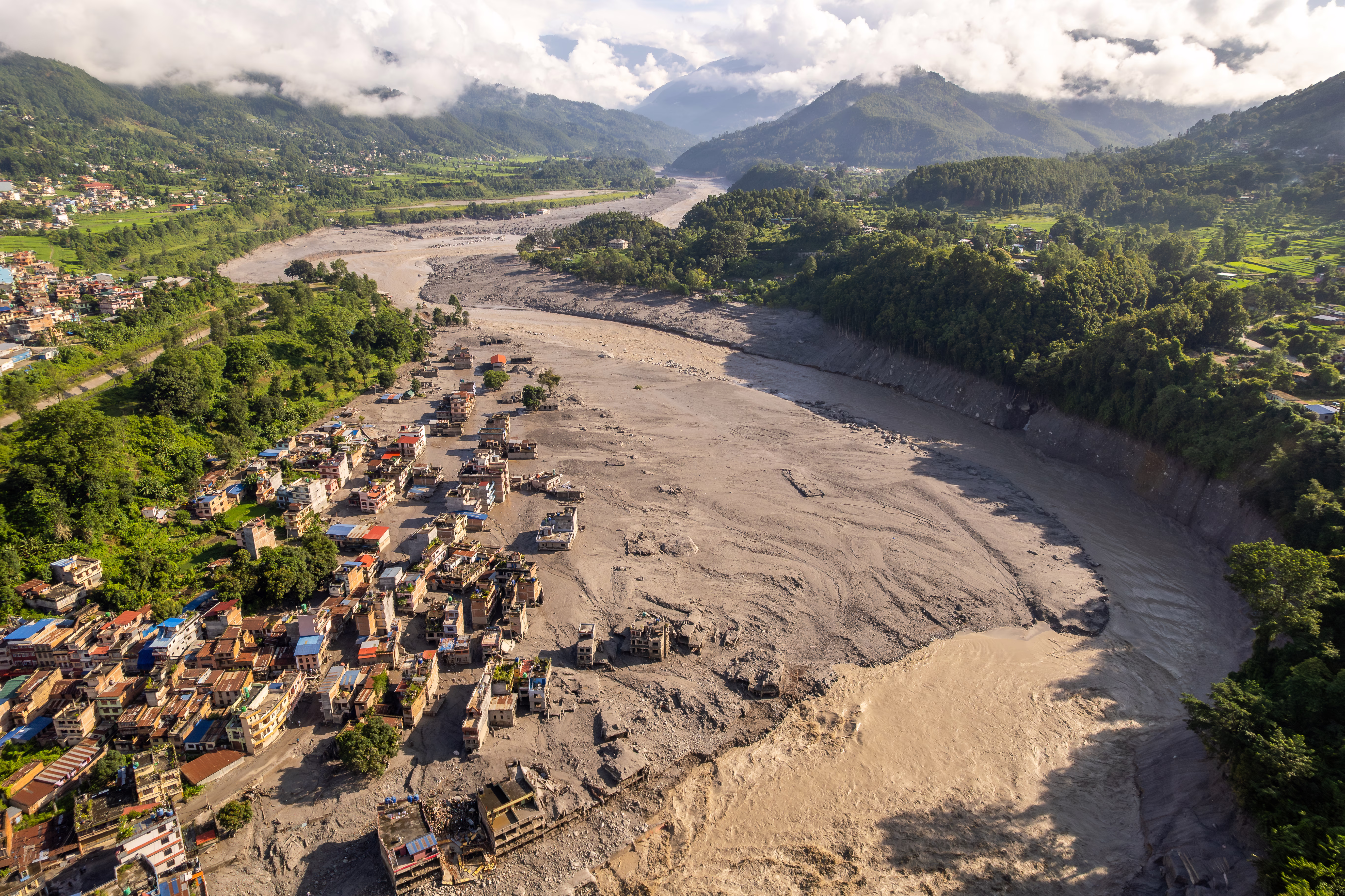 An aerial view of dmaged houses and debris deposits along a recently-flooded river