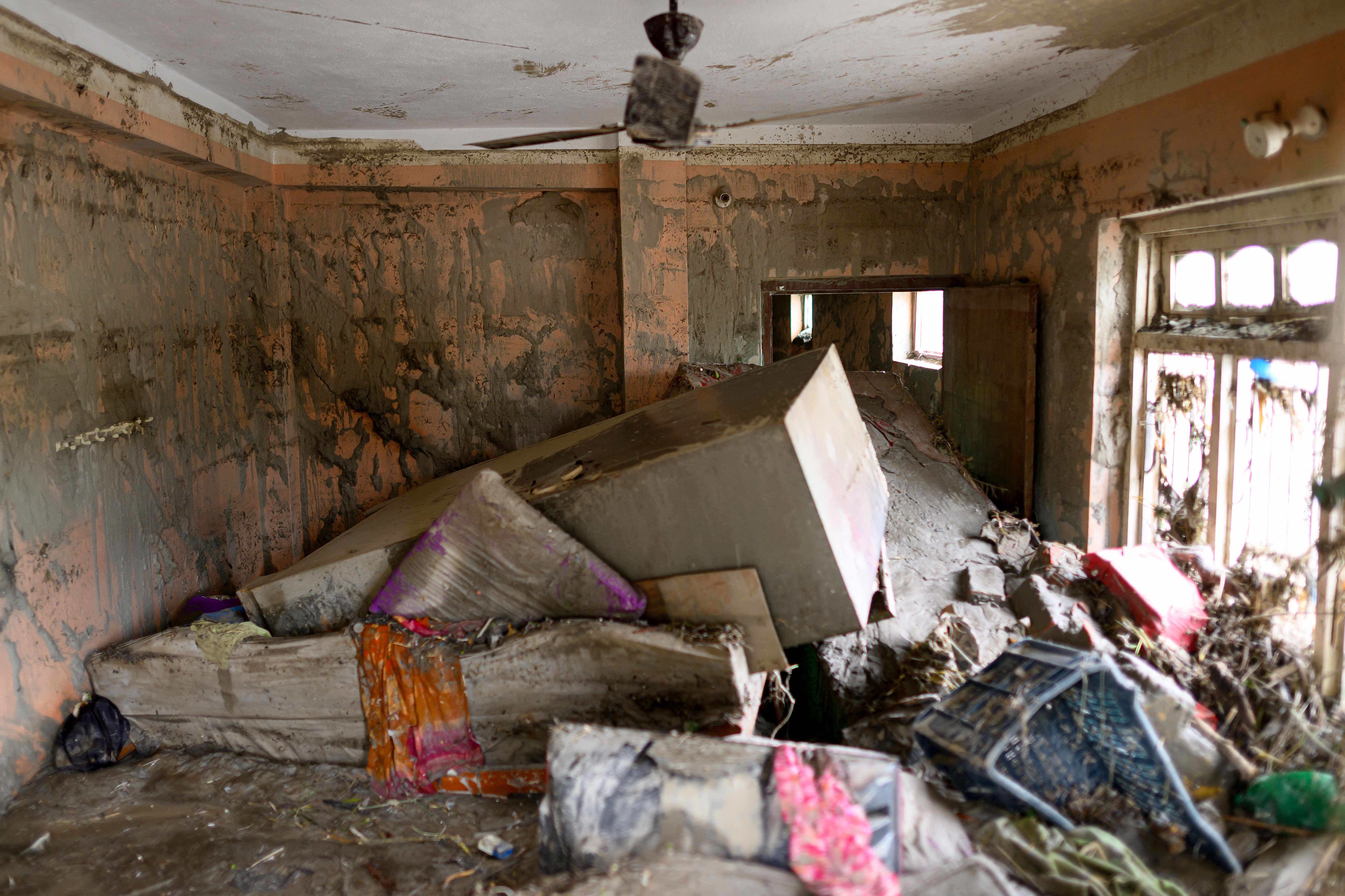 A room inside a house, filled with toppled and mud-covered furniture and belongings