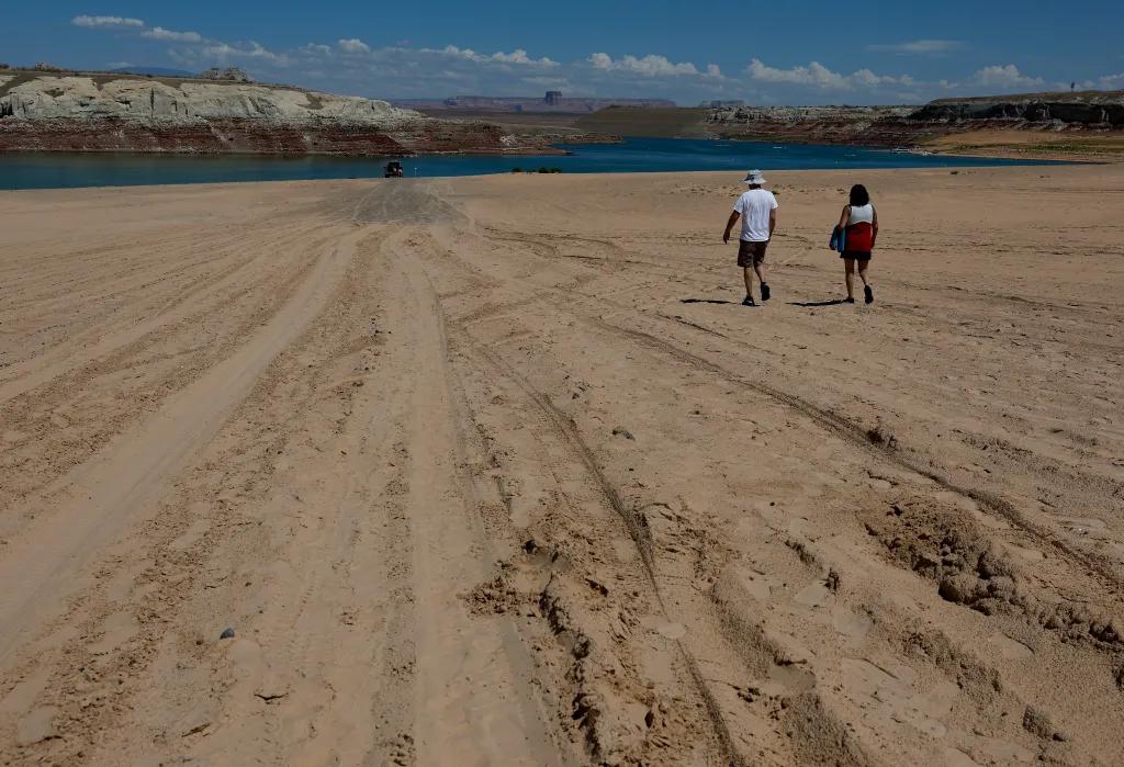 Two park visitors walk on an area of Lake Powell that was previously underwater at Lone Rock Beach.