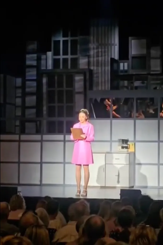 Karla Tracey, dressed as Dolly Parton's character, Doralee, addresses the audience on stage.