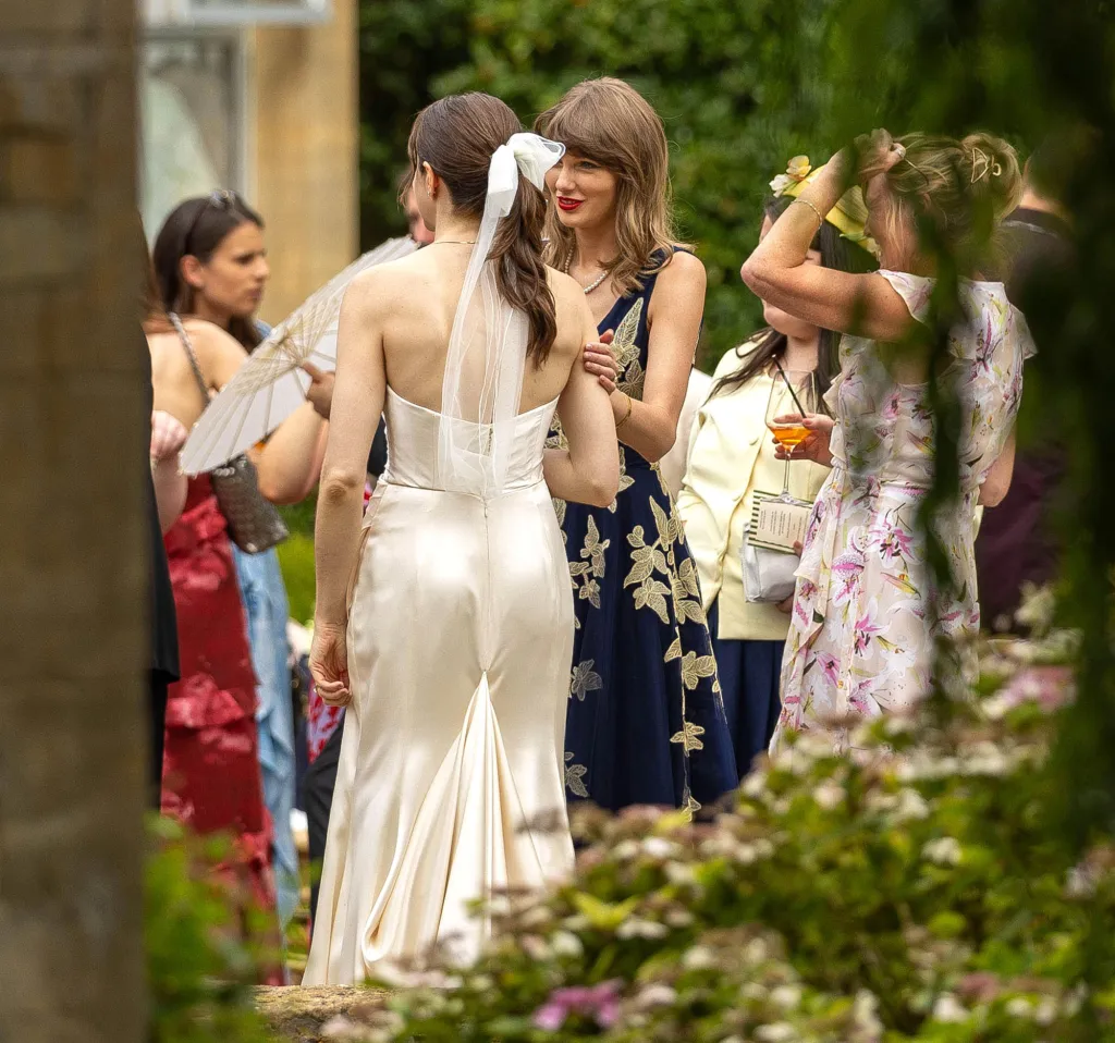 Taylor Swift in a navy dress with gold embroidery stands next to Laura Sisk in a white wedding gown and veil at her wedding.