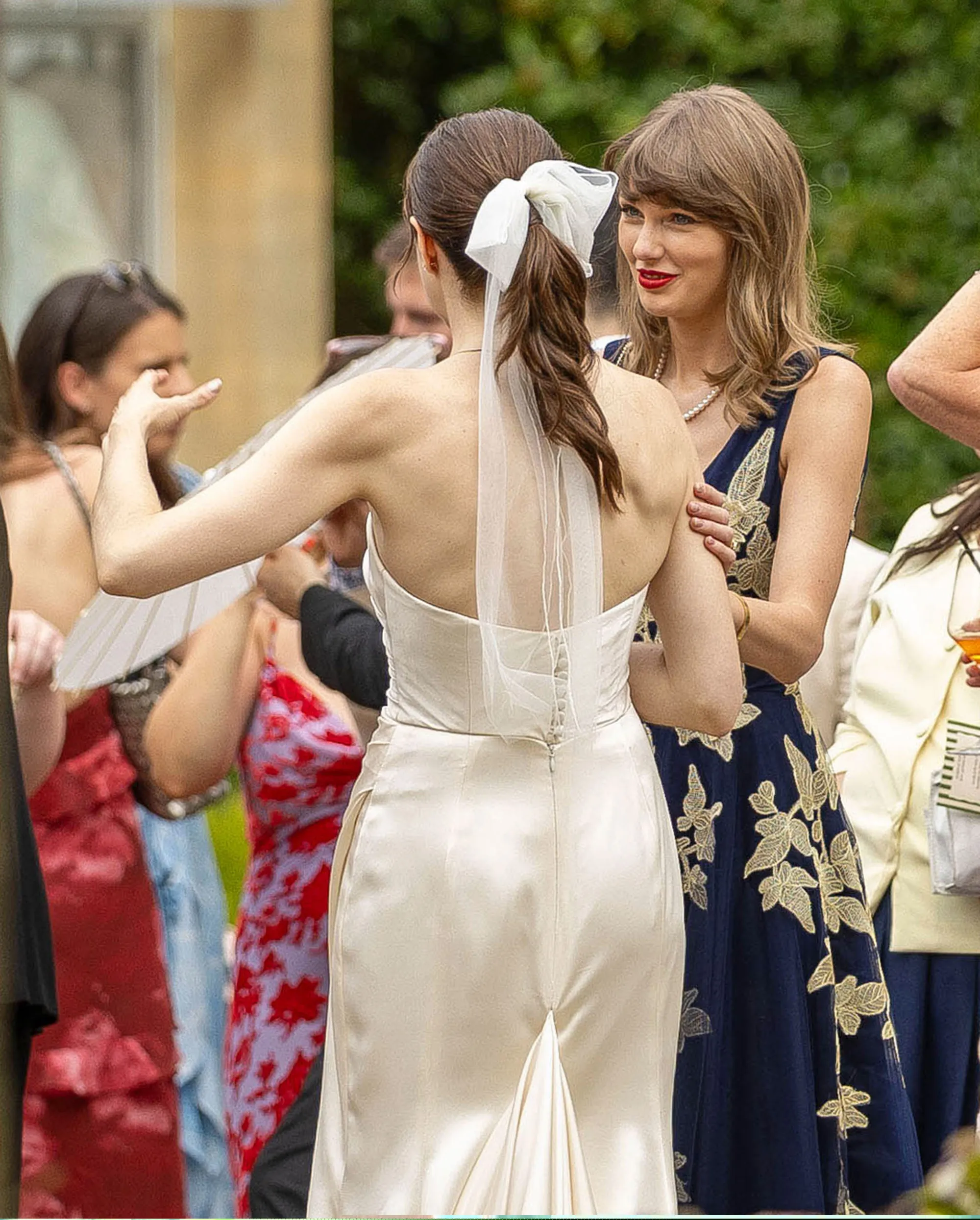 Taylor Swift, in a navy dress with gold embroidery, talking to Laura Sisk, the bride, in a white gown with a bow and veil.