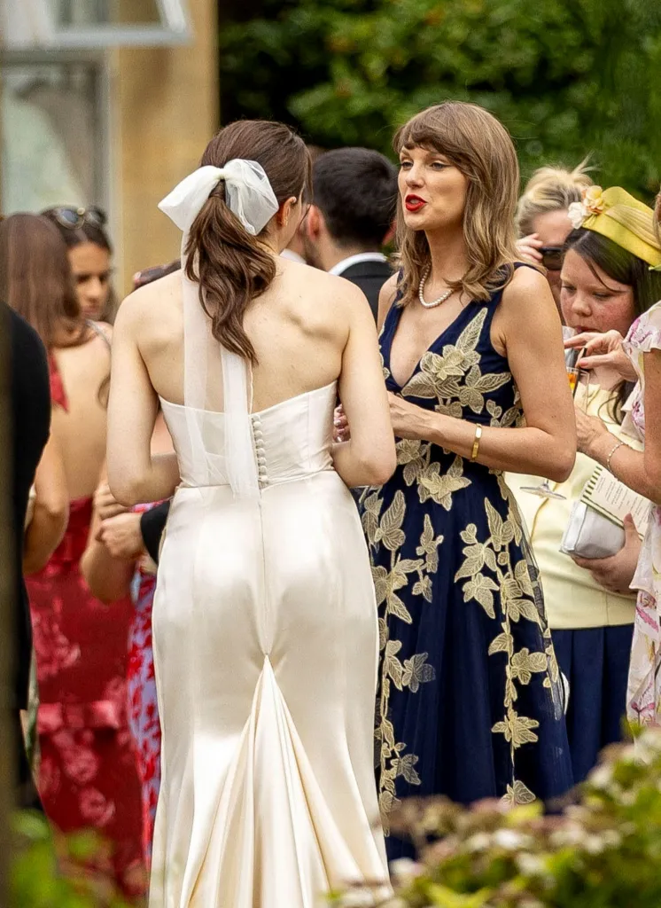 Taylor Swift in a navy blue and gold embroidered dress talking to a woman in a white wedding dress.