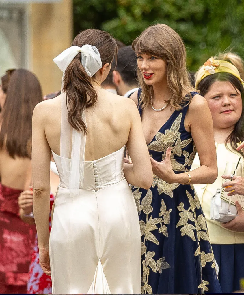 Taylor Swift in a navy dress with gold embroidery speaks to Laura Sisk in a white wedding gown.