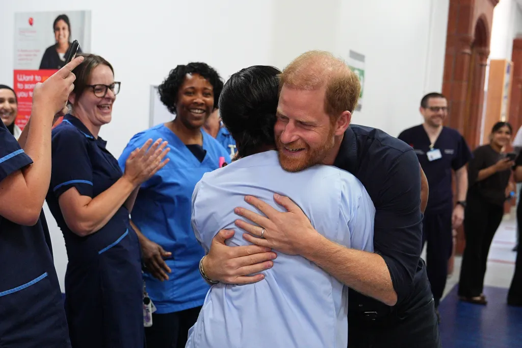 Prince Harry, in a black shirt, embracing a WellChild nurse at Birmingham Children's Hospital.